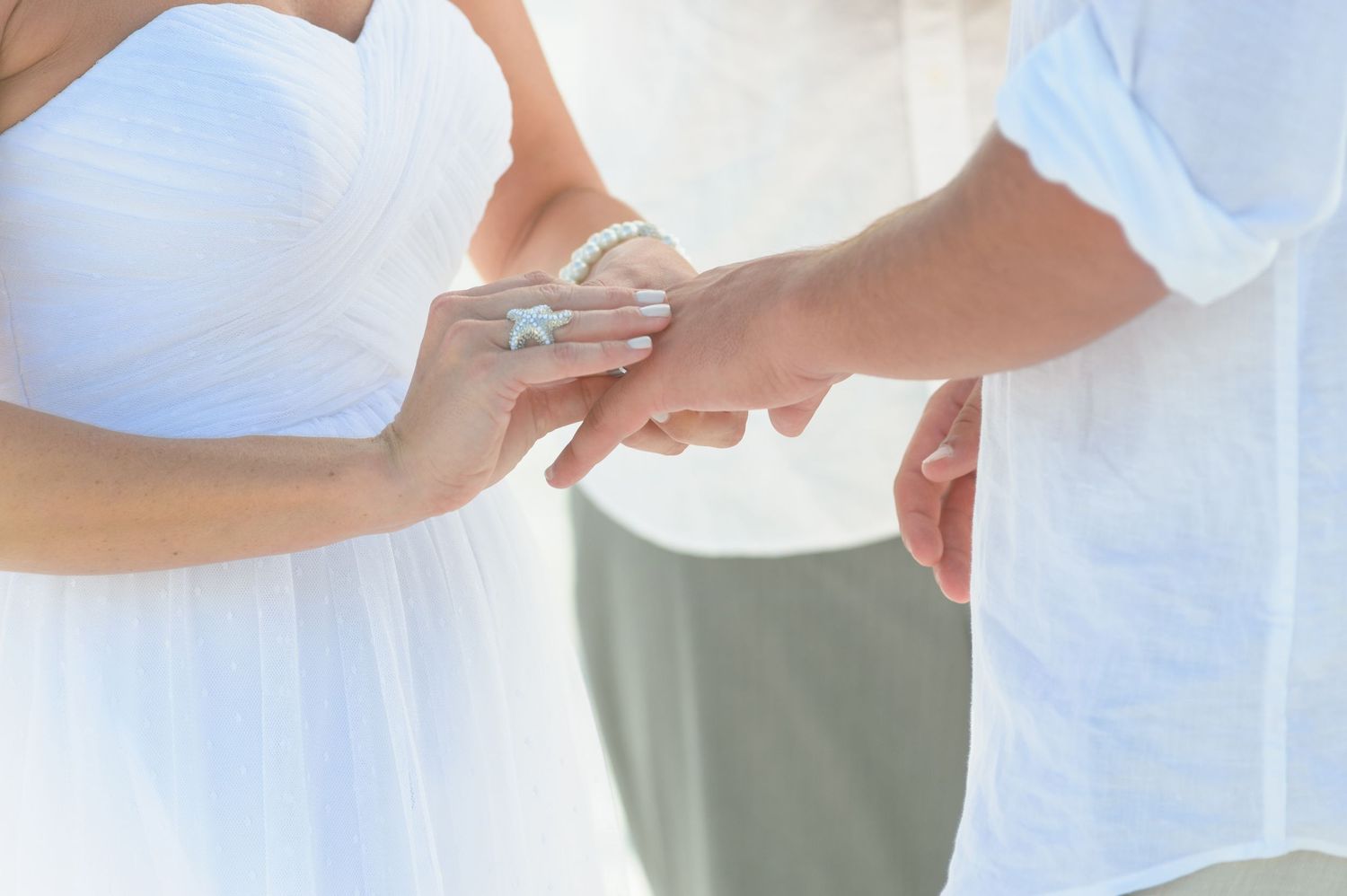 Close-up of bride placing wedding ring on grooms hand during beach wedding ceremony.