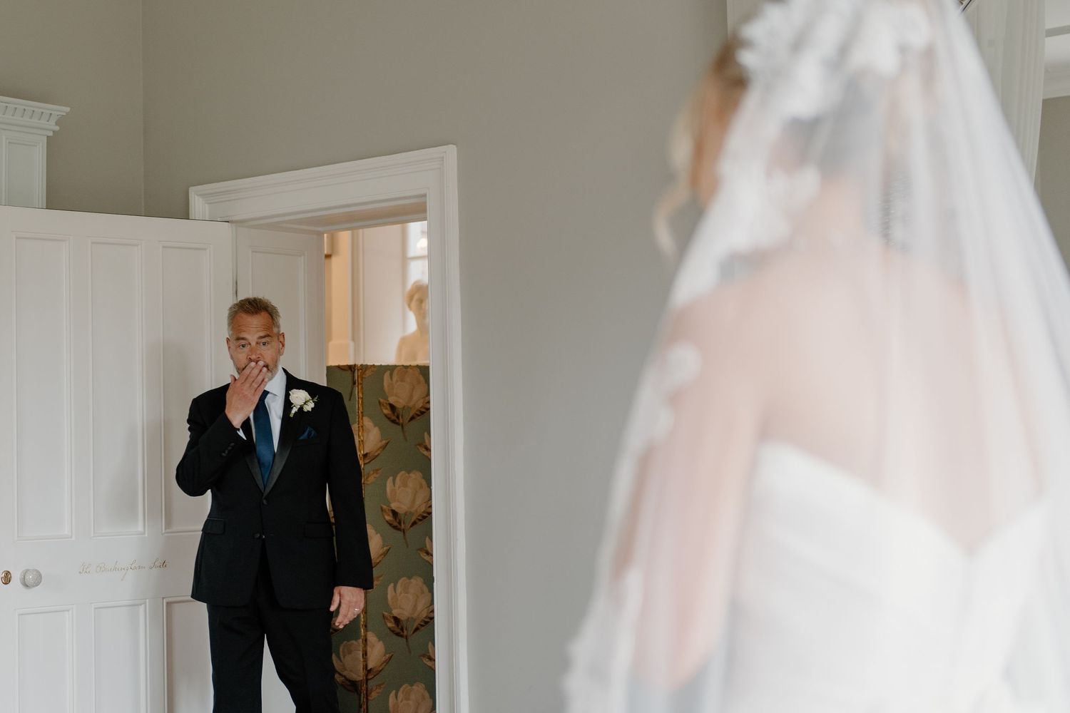 Emotional father in black suit reacting to seeing his daughter in her wedding dress for the first time.
