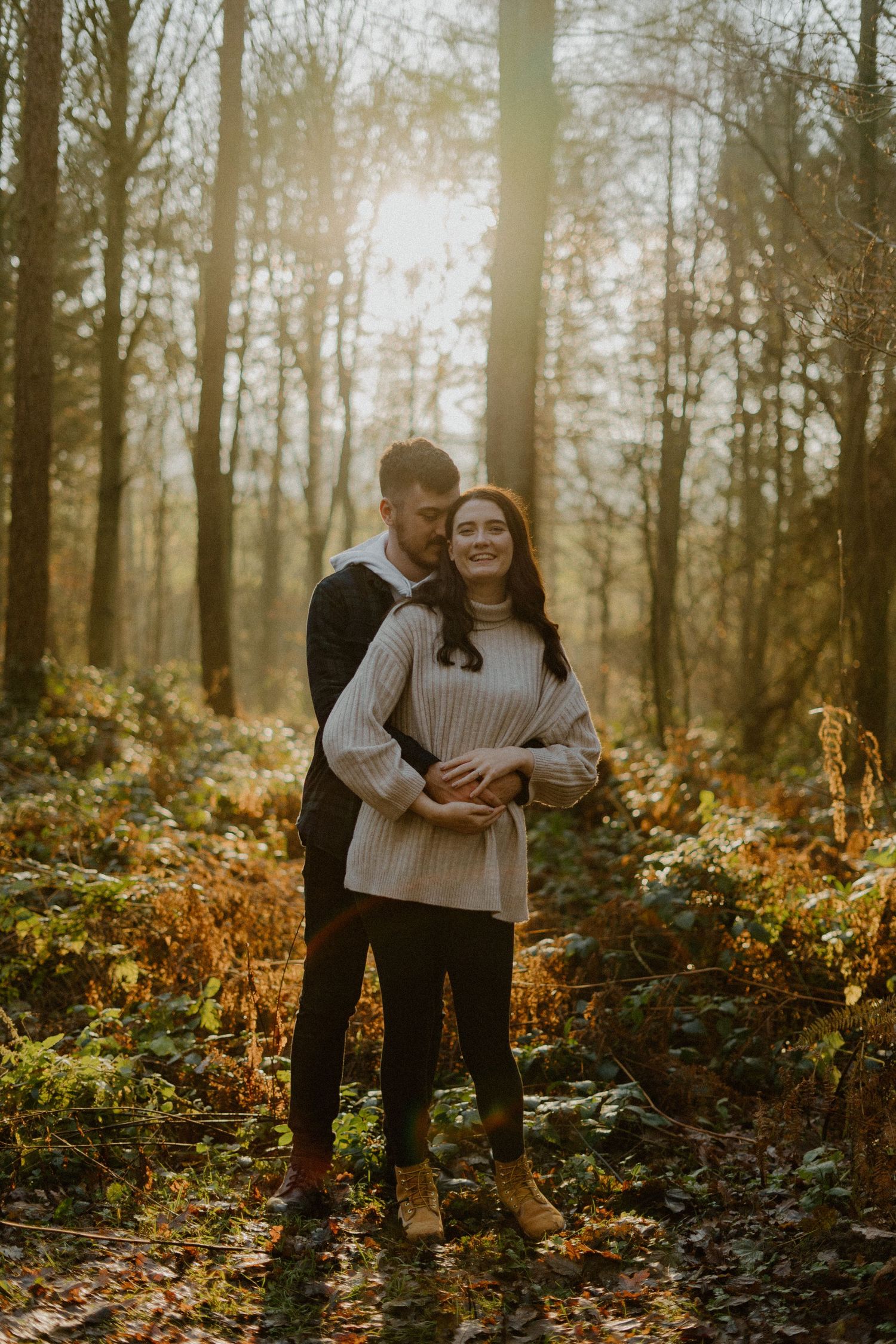 Happy couple embracing in sunlit autumn forest, golden hour light filtering through trees.