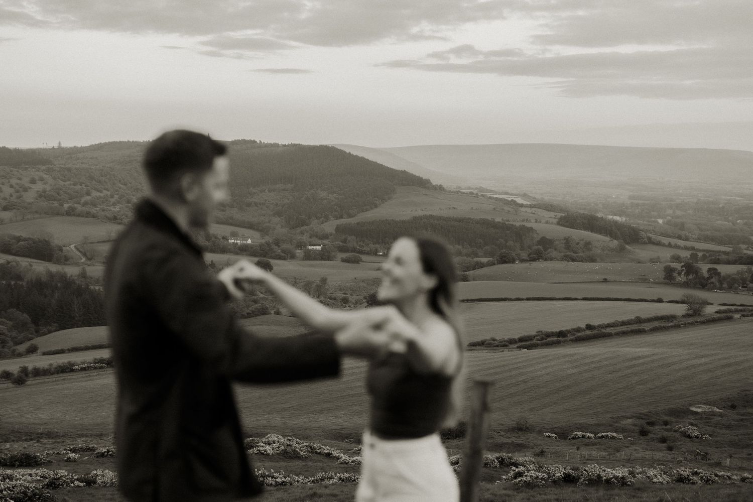 Black and white romantic couple dancing with scenic valley landscape in background.