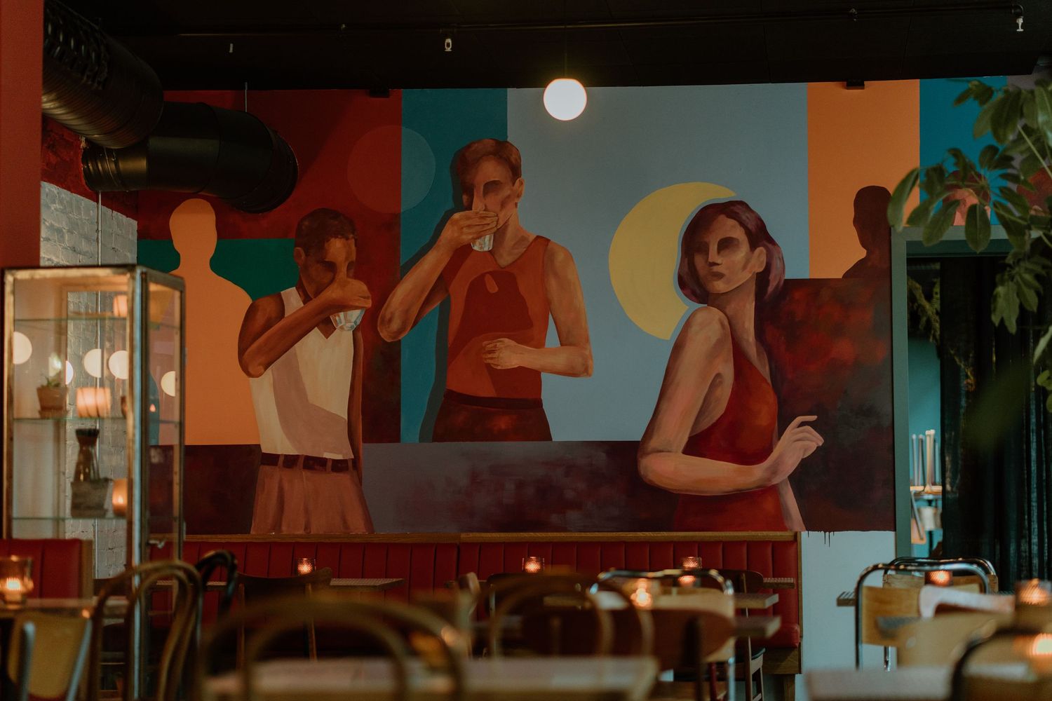 A large wall mural inside a restaurant depicts a retro-style scene with people enjoying drinks in warm lighting.