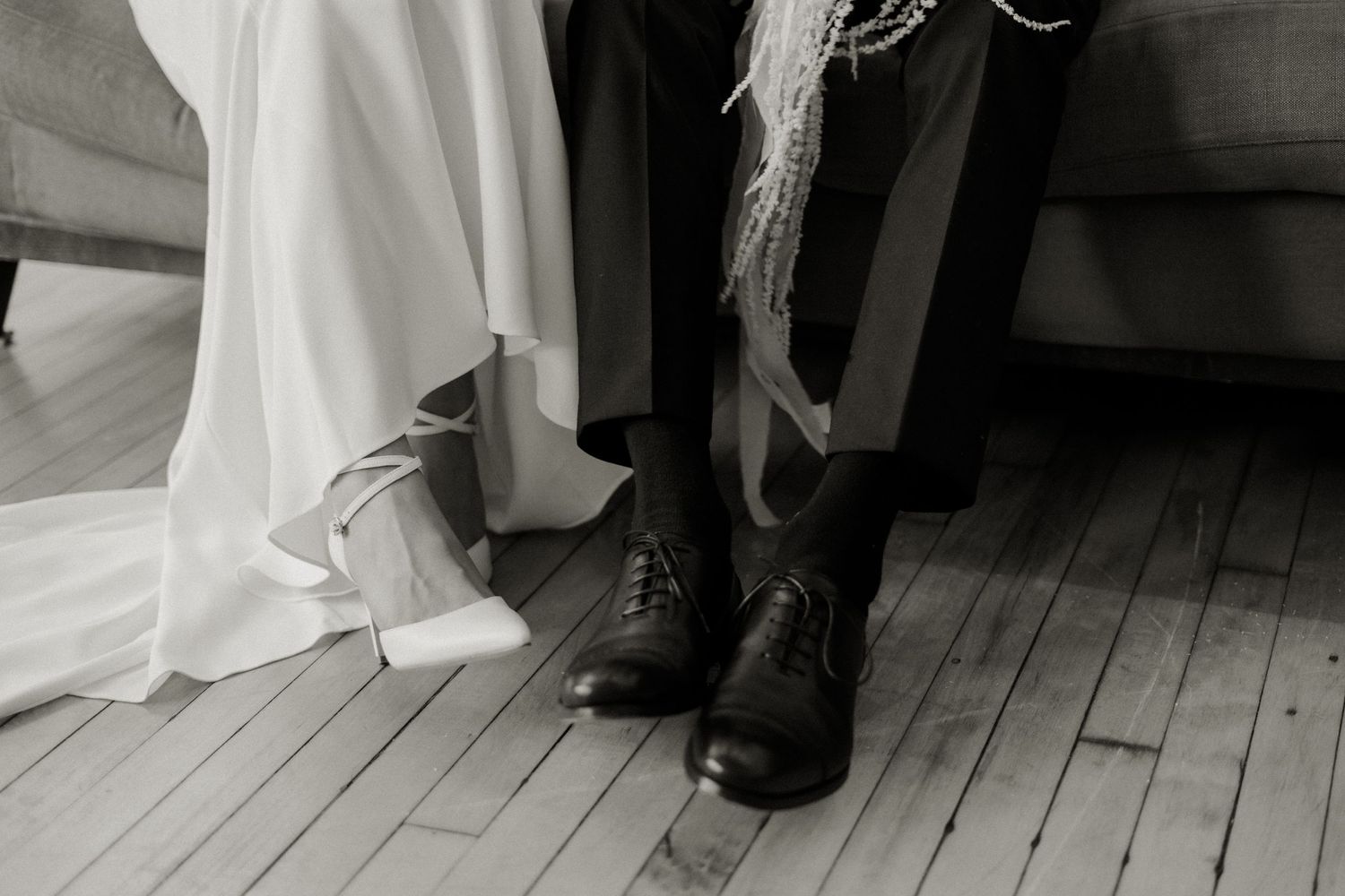 Black and white photo of bride and groom's shoes on wooden floorboards.