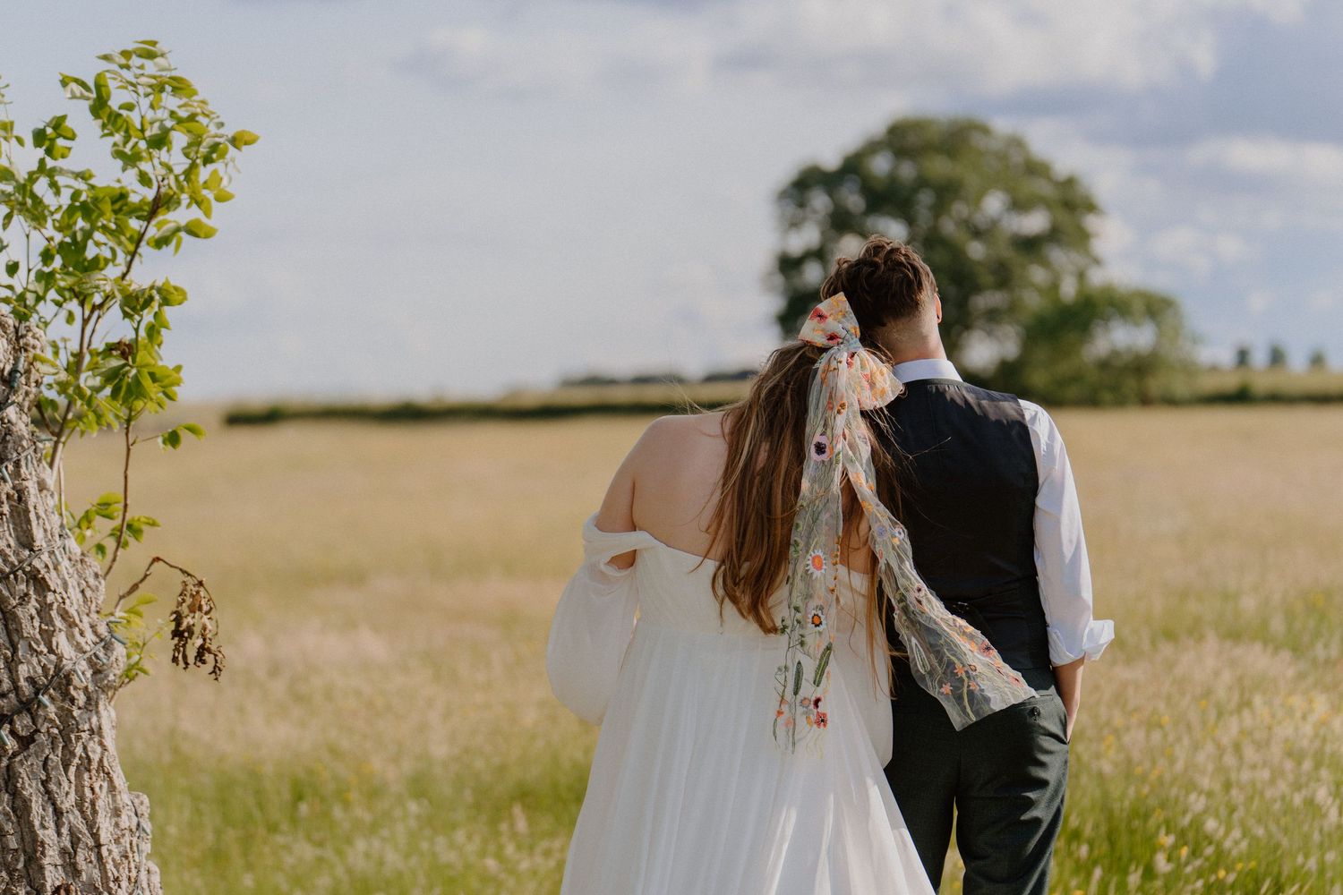 Bride and groom walking away through golden wheat field on a bright summer wedding day.