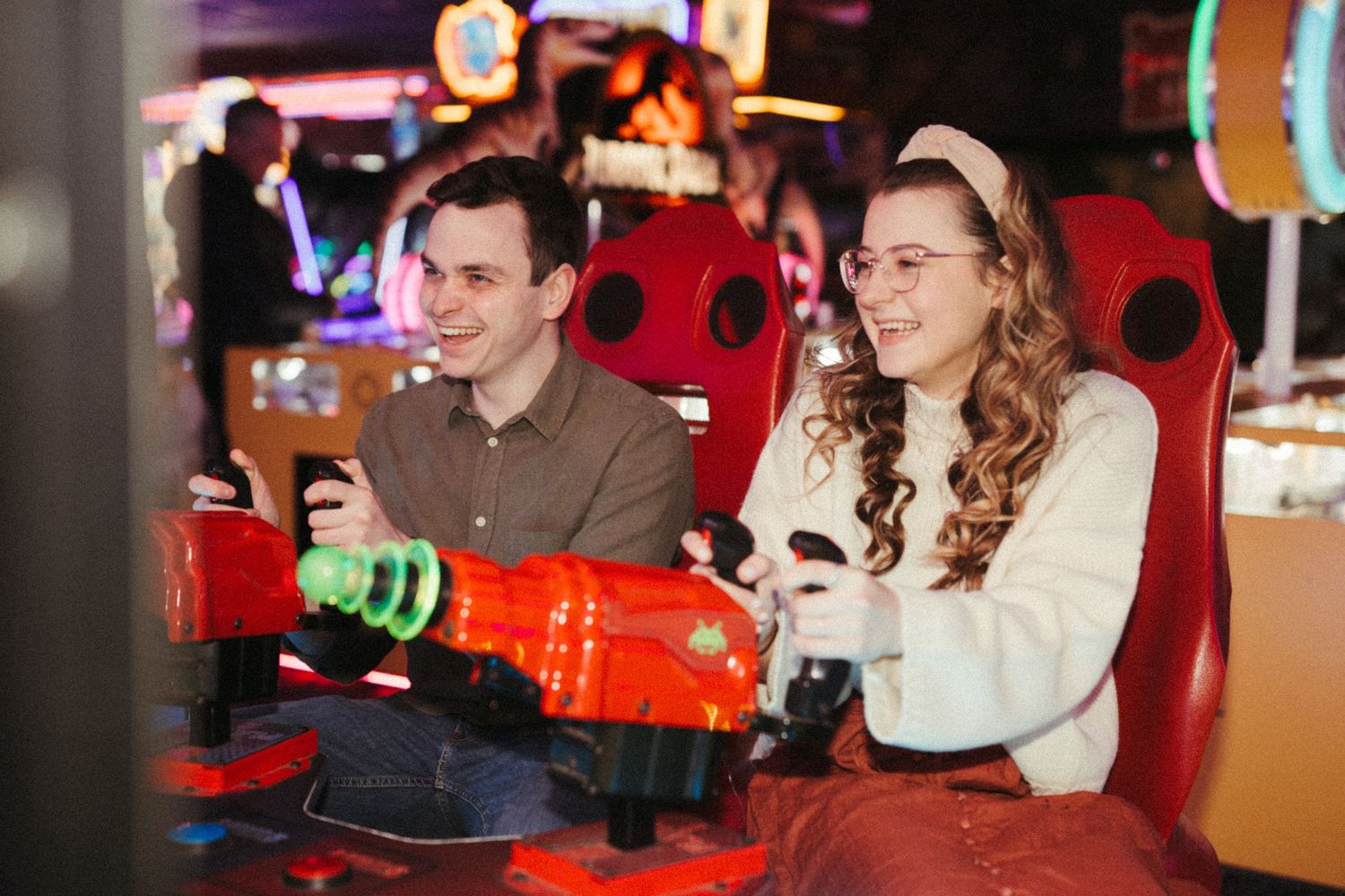 A couple enjoys playing arcade games together in a colorful gaming venue with red ladybug-themed seats.