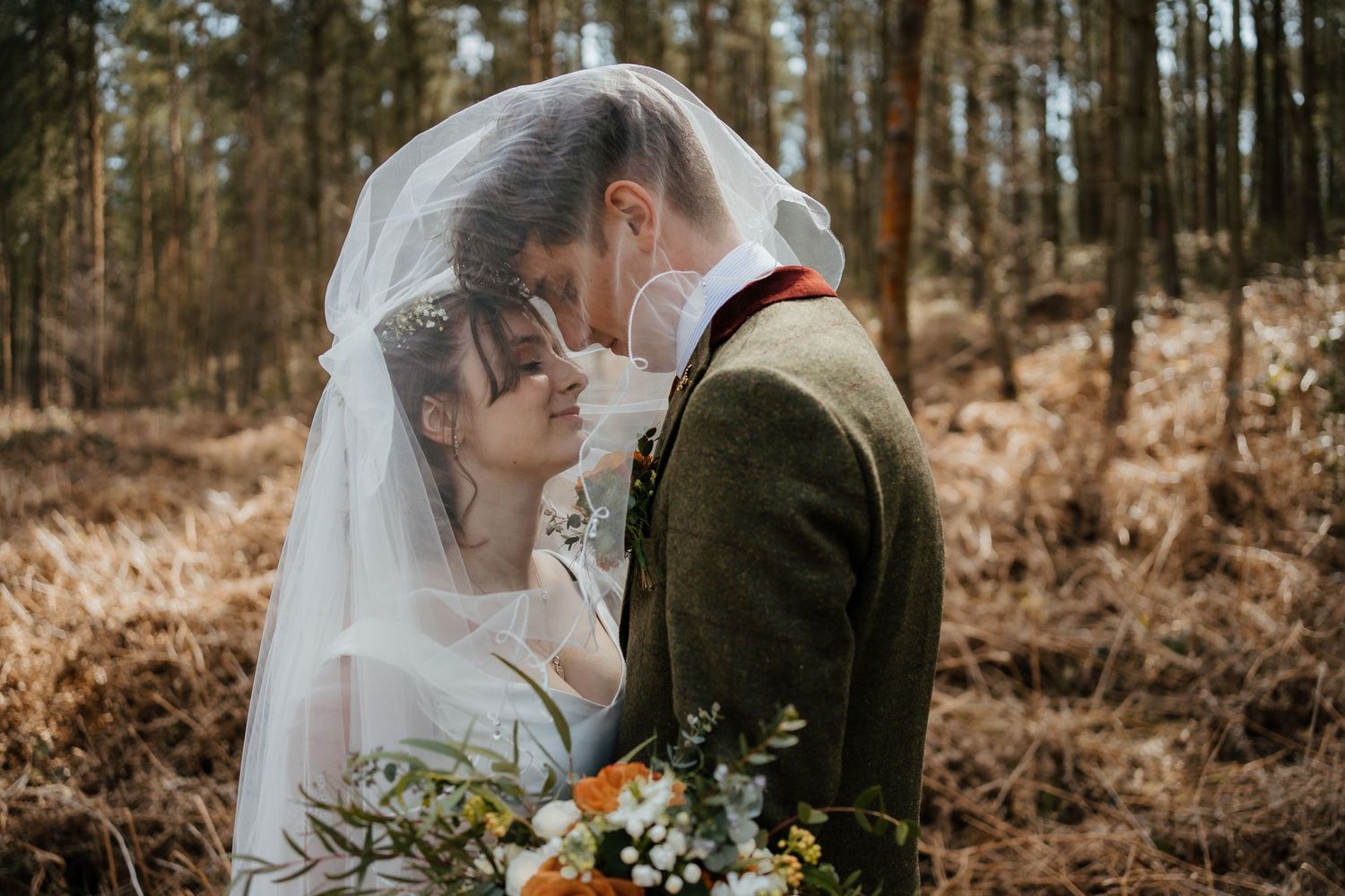 A tender outdoor winter wedding moment with evergreen trees in the background.
