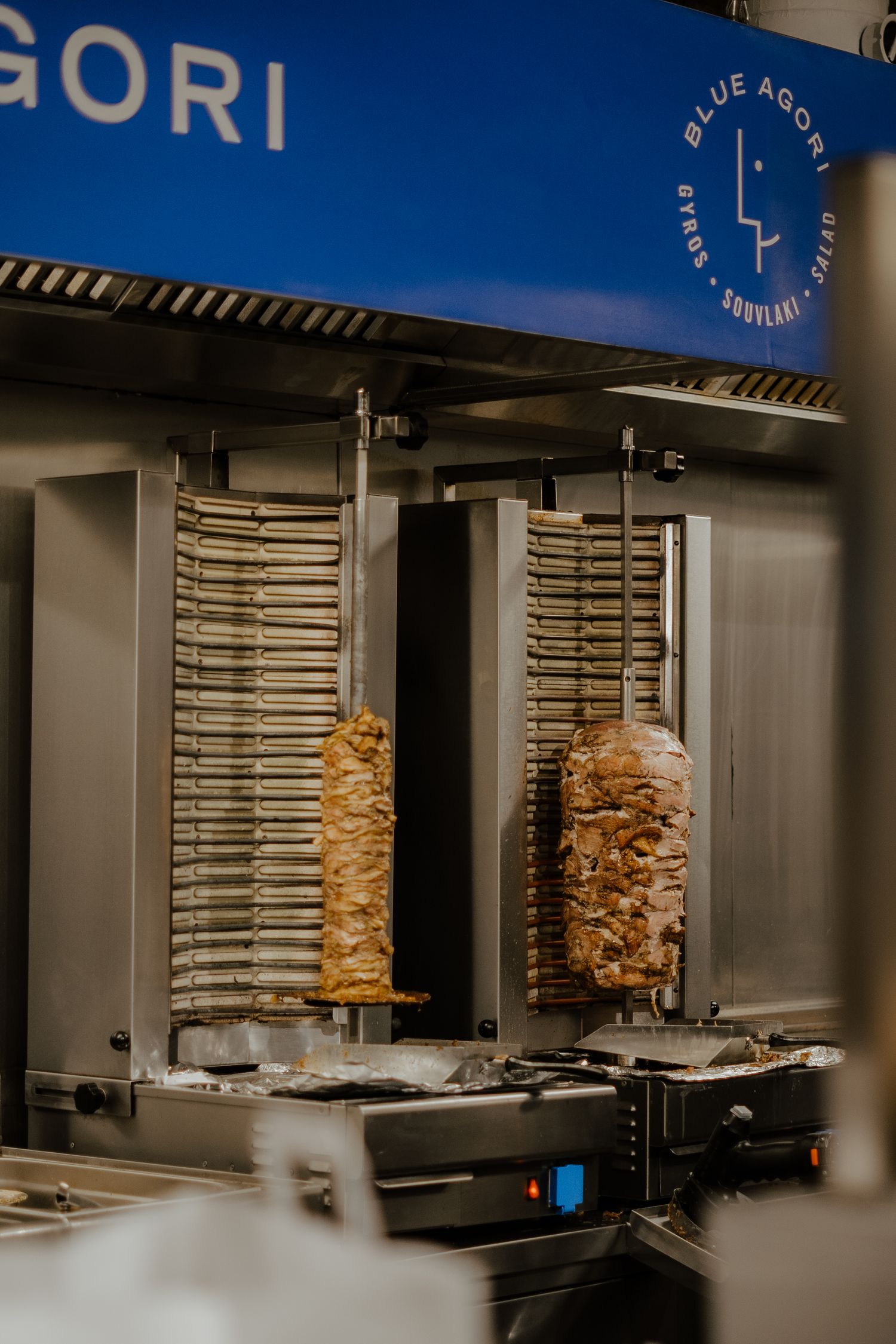 Vertical rotisserie spits with stacks of marinated meat rotating in a commercial kitchen setting.