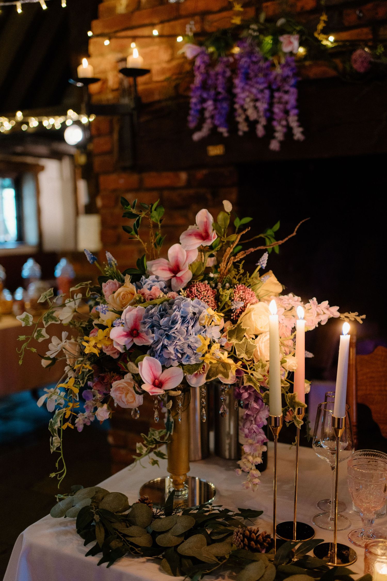 A beautiful tall floral centerpiece with pink magnolias and blue hydrangeas surrounded by candles.