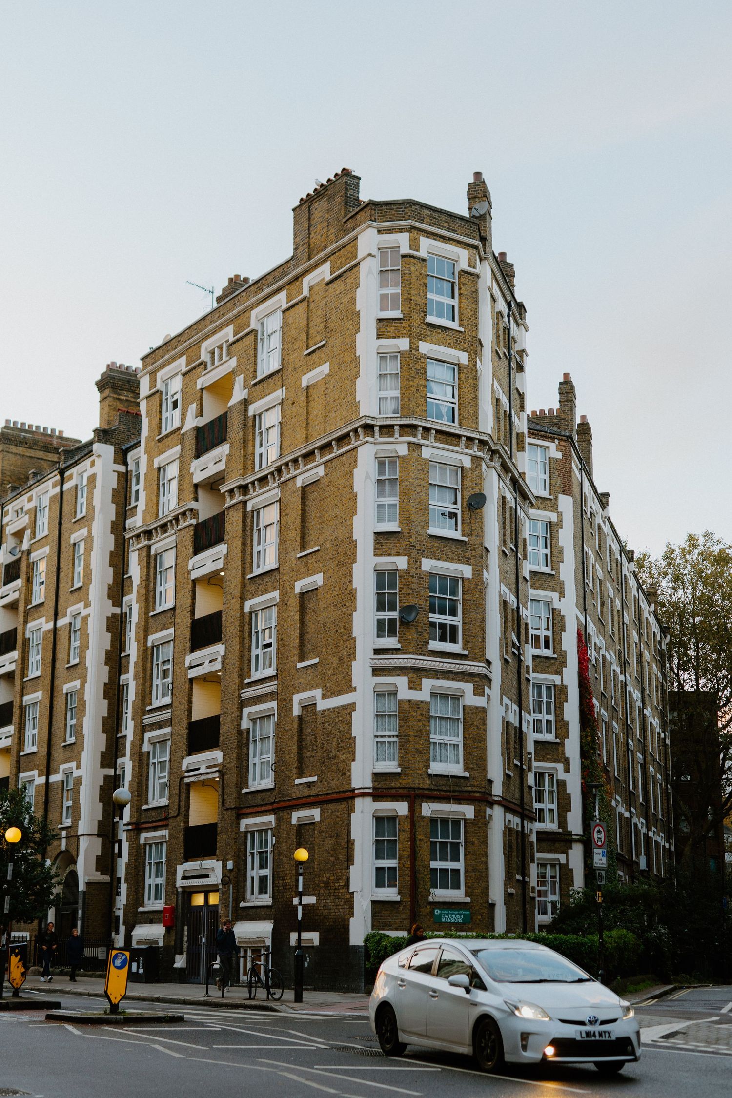 Classic Victorian brick corner building in London with white trim windows and a white car passing by.