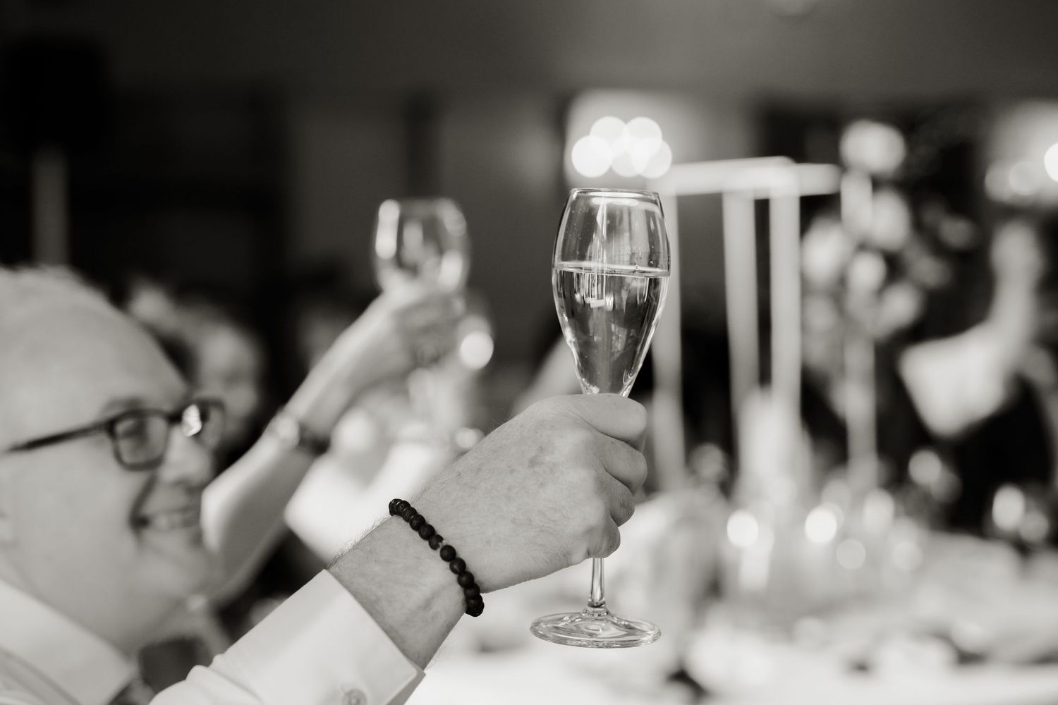 Black and white photo of wedding guests raising champagne glasses in a celebratory toast.