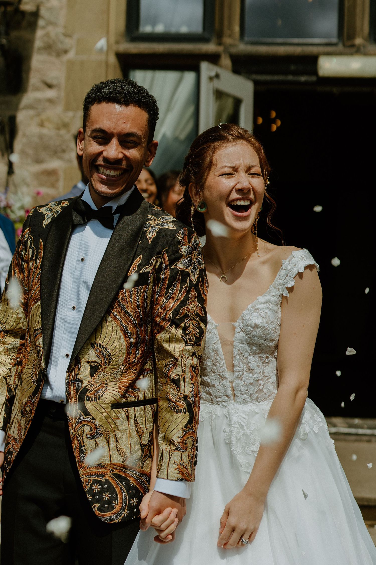 Bride and groom laughing joyfully as confetti falls outside during wedding celebration.