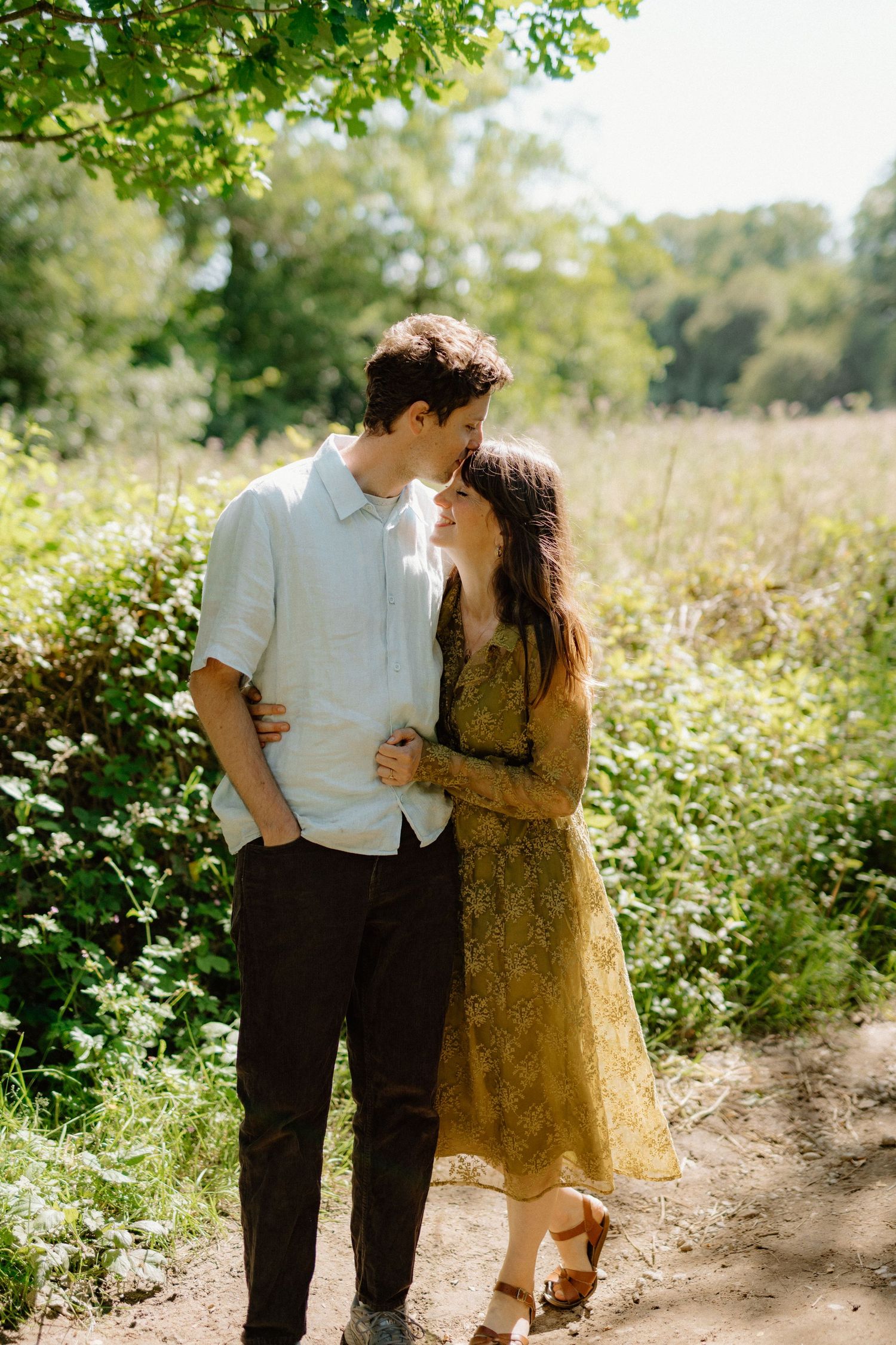 Young couple sharing a tender moment on a sunny nature trail surrounded by greenery.