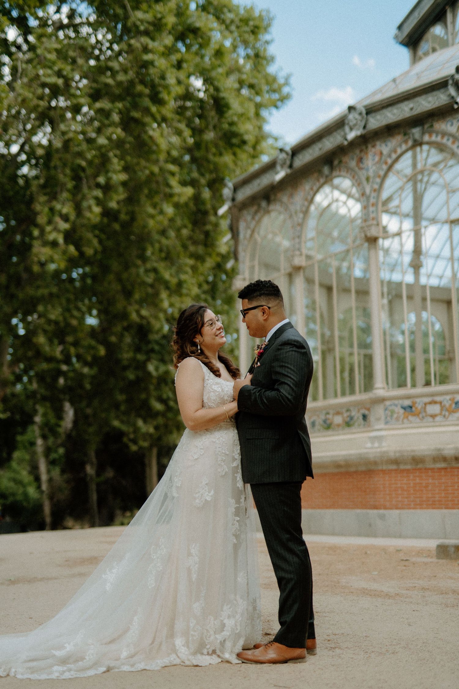 Smiling couple in wedding attire share tender moment before ornate crystal palace greenhouse.