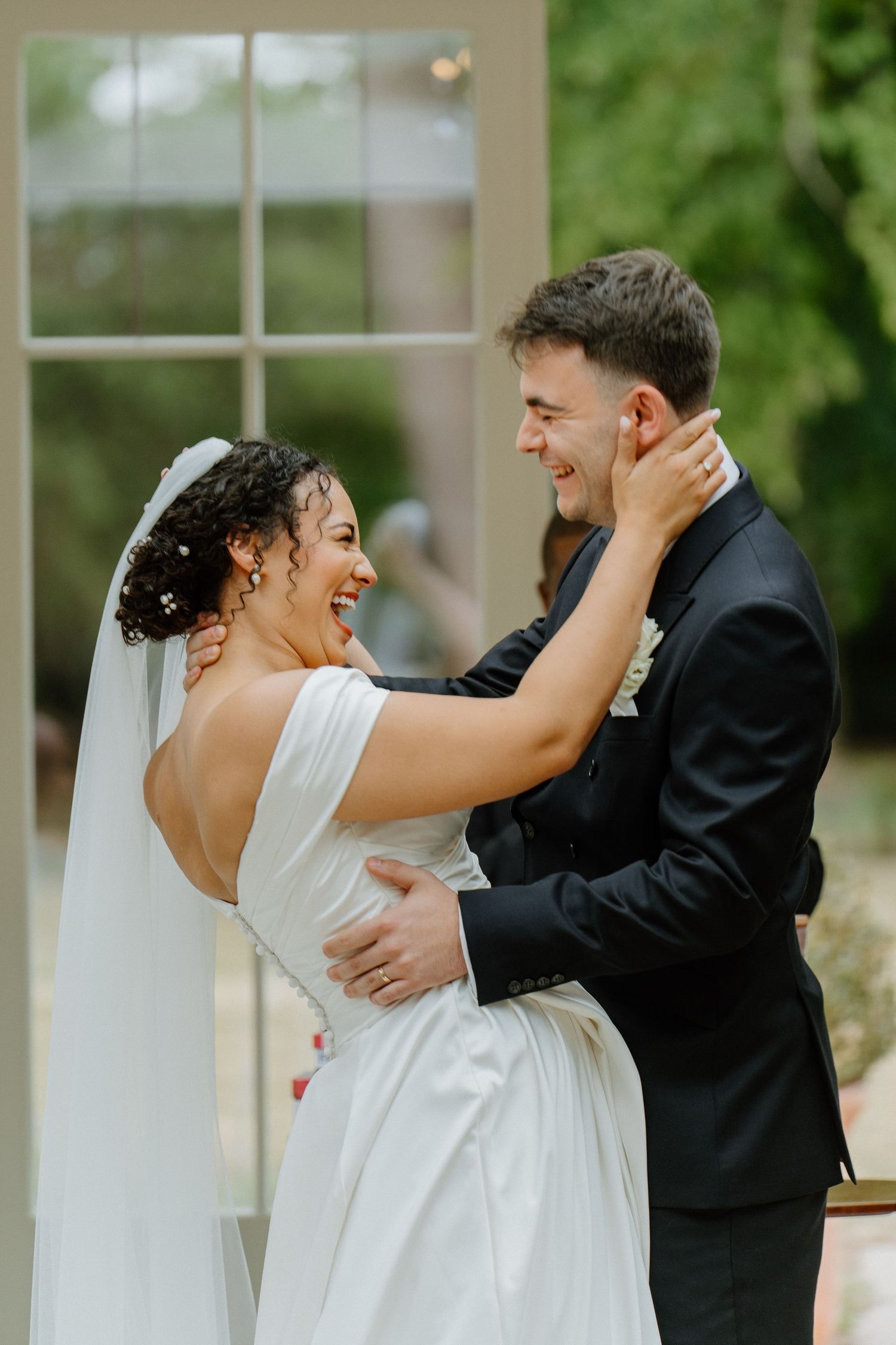 Bride in white gown and groom in black suit embracing and laughing.