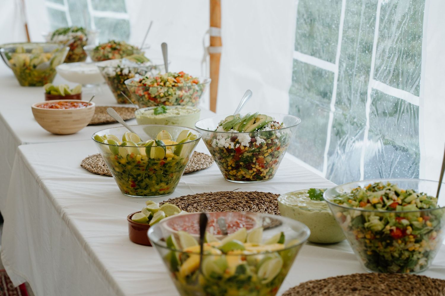 Elegant wedding buffet table with assorted fresh salads in glass bowls under a white tent.
