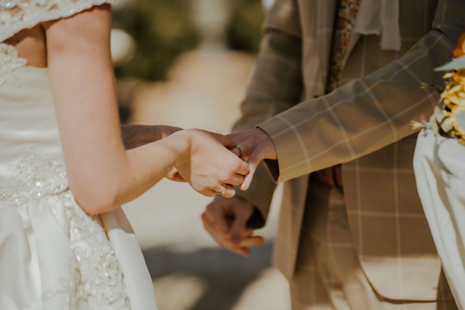 Close-up of bride and groom holding hands during outdoor wedding ceremony, groom in plaid suit.