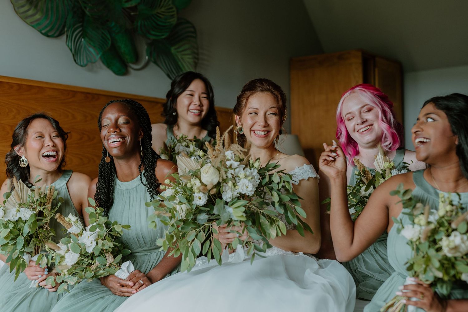 Joyful bride with diverse bridesmaids in mint dresses holding white and green bouquets.