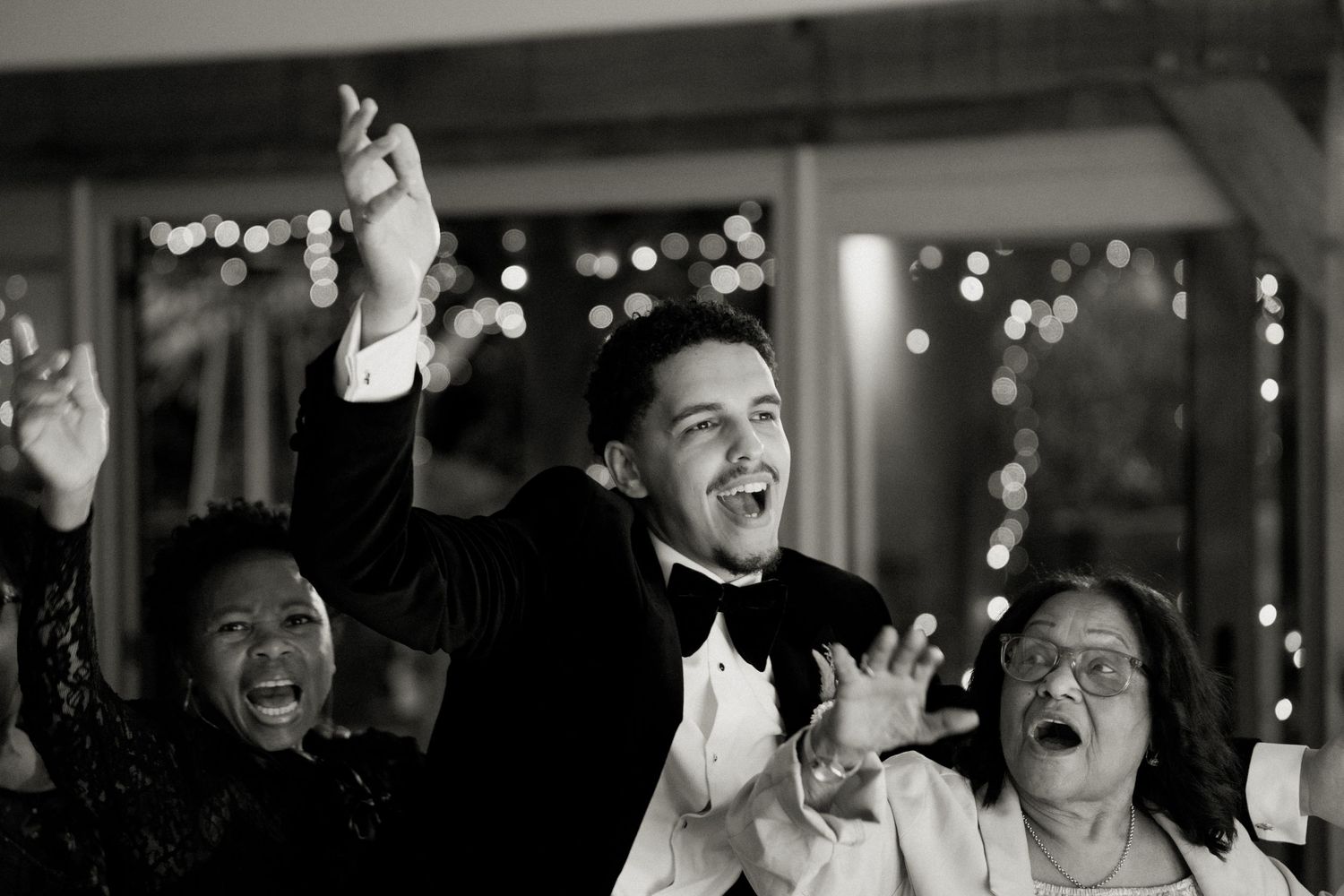 Black and white photo of groom celebrating enthusiastically with guests on the dance floor.