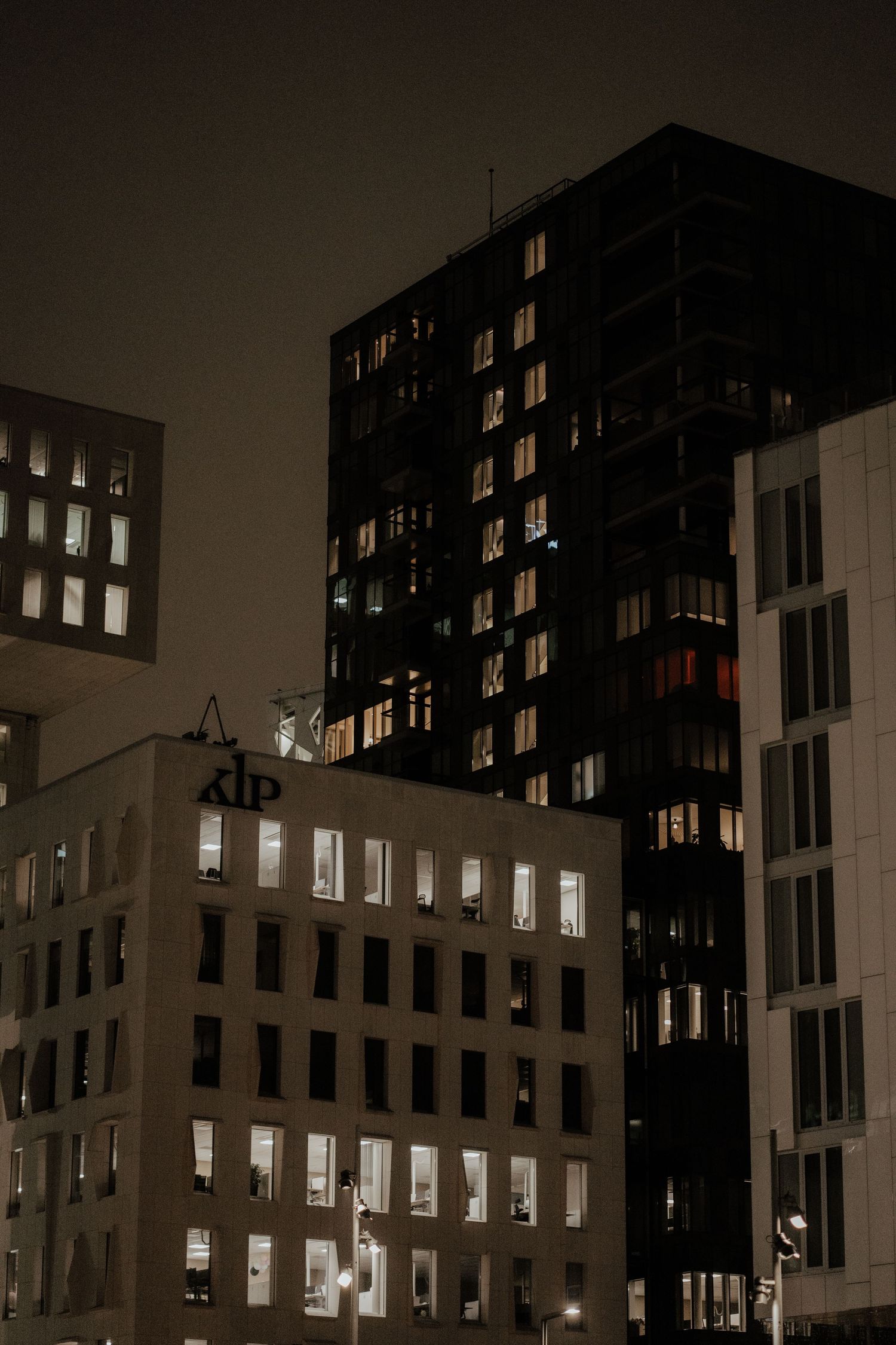 Dark urban cityscape at night with illuminated windows in tall apartment buildings creating a moody atmosphere.
