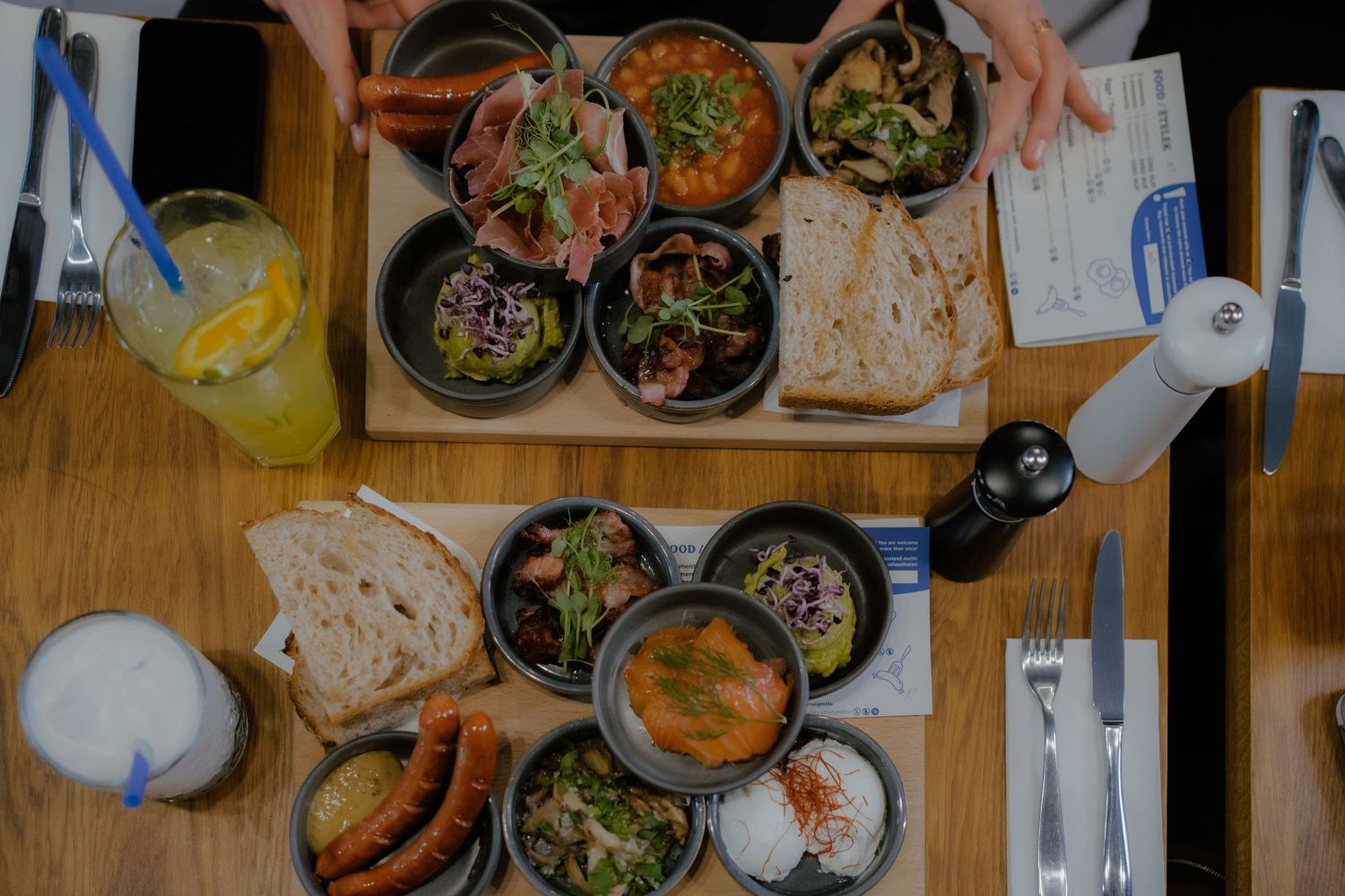 Overhead view of various dishes and bowls on a wooden table with bread and drinks during a casual dining setting.