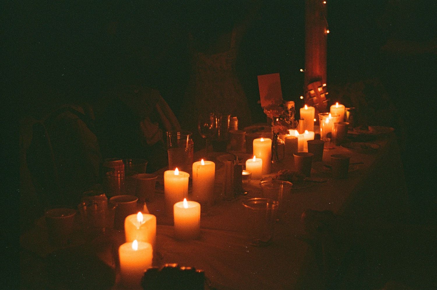 Romantic candlelit wedding reception table with glowing white pillar candles in warm dim light.