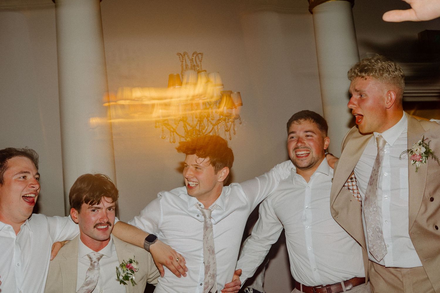 Groomsmen laughing and celebrating together at a wedding reception in a elegant venue.