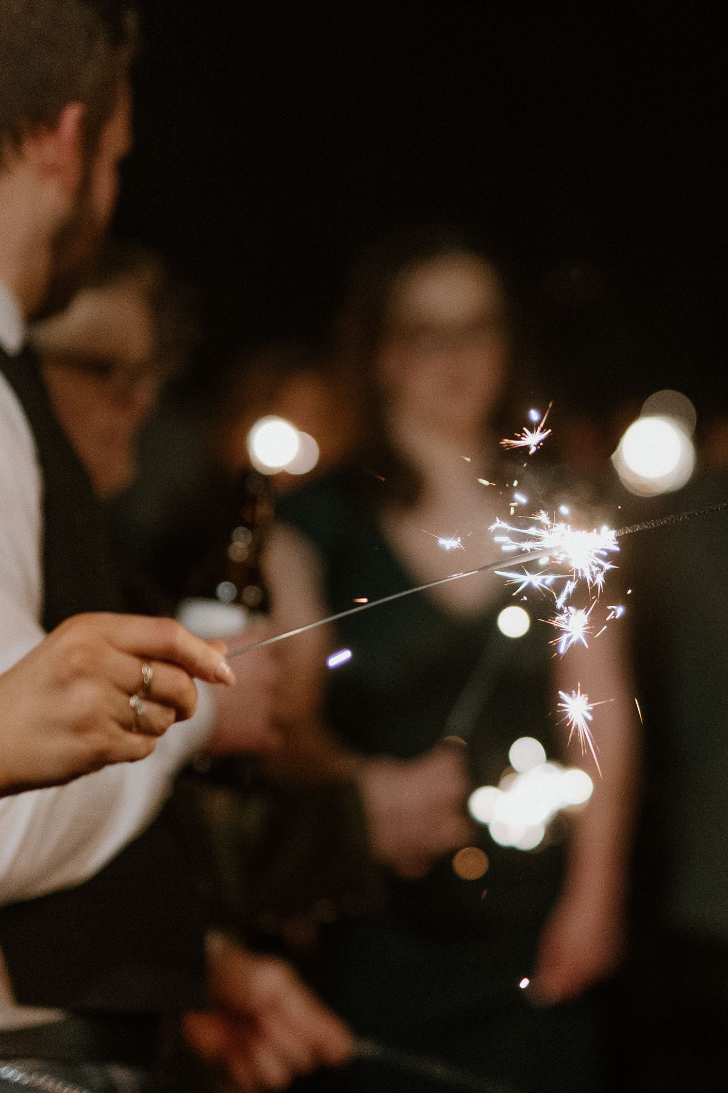 Wedding guest holding a sparkling sparkler in the dark during a romantic nighttime wedding sendoff.