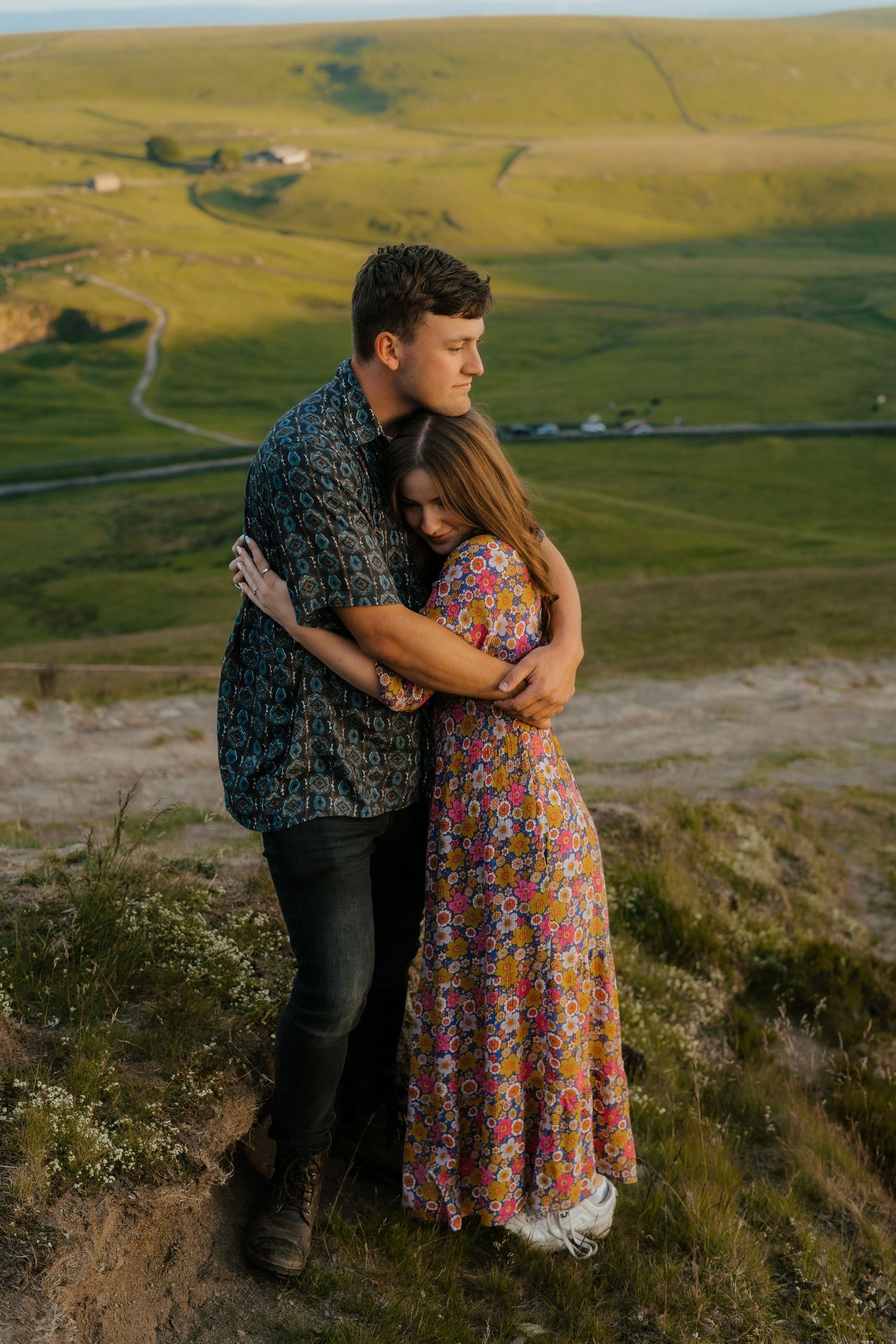 Couple embracing tenderly on a hilltop overlooking lush green rolling countryside valleys.