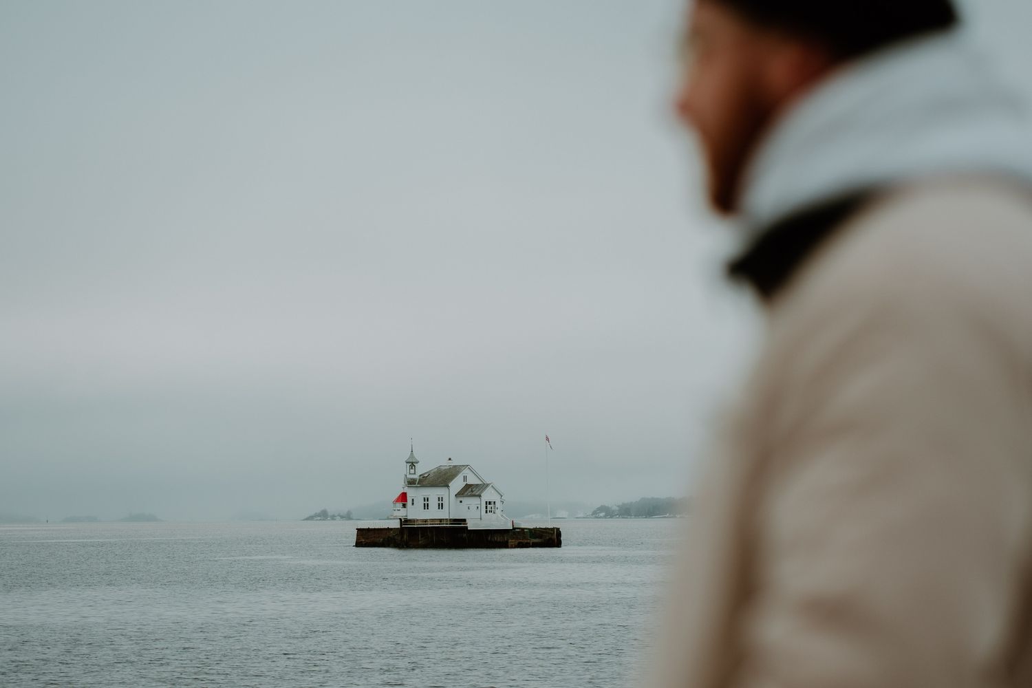 Silhouette of a lighthouse on a foggy sea with a blurred figure in the foreground.
