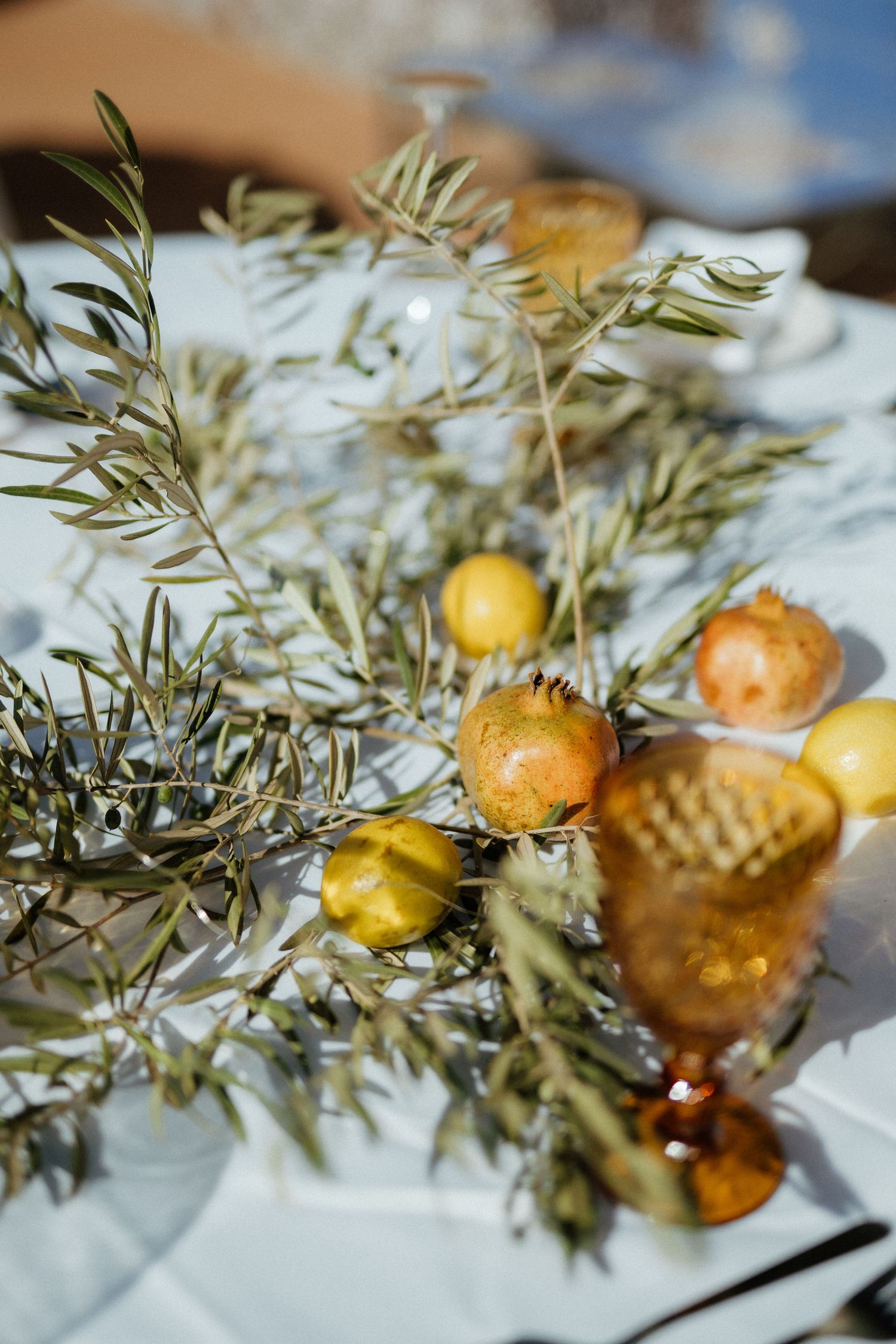 Elegant wedding table centerpiece with olive branches, lemons, and pomegranates on white linen.
