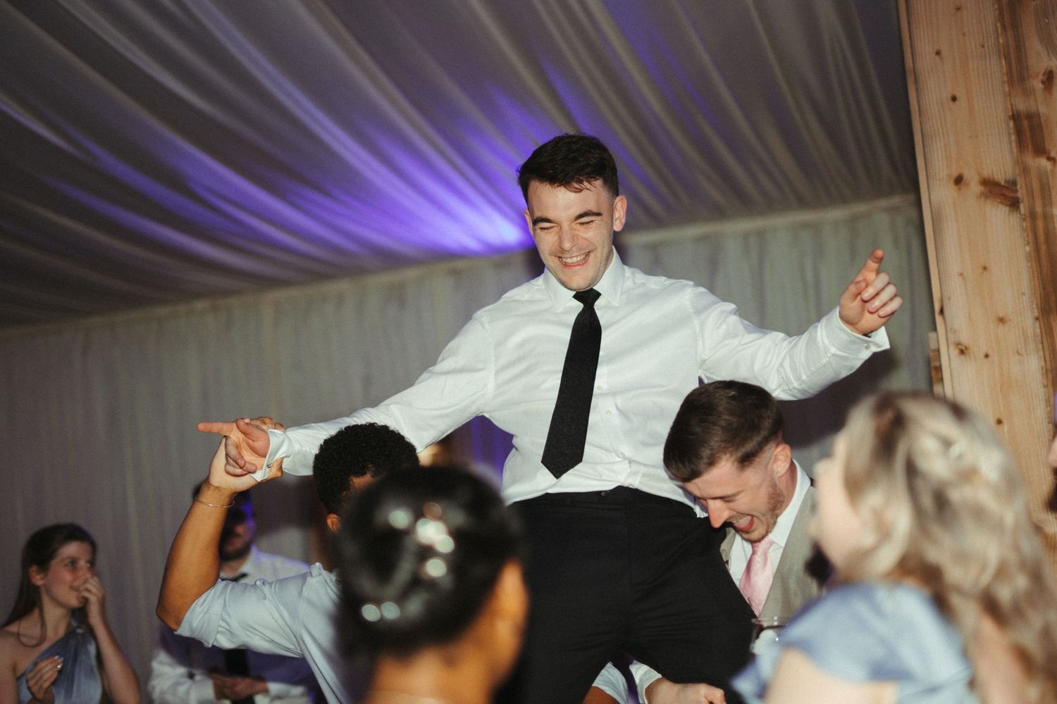 Groom lifted by groomsmen on the dance floor during lively wedding reception.