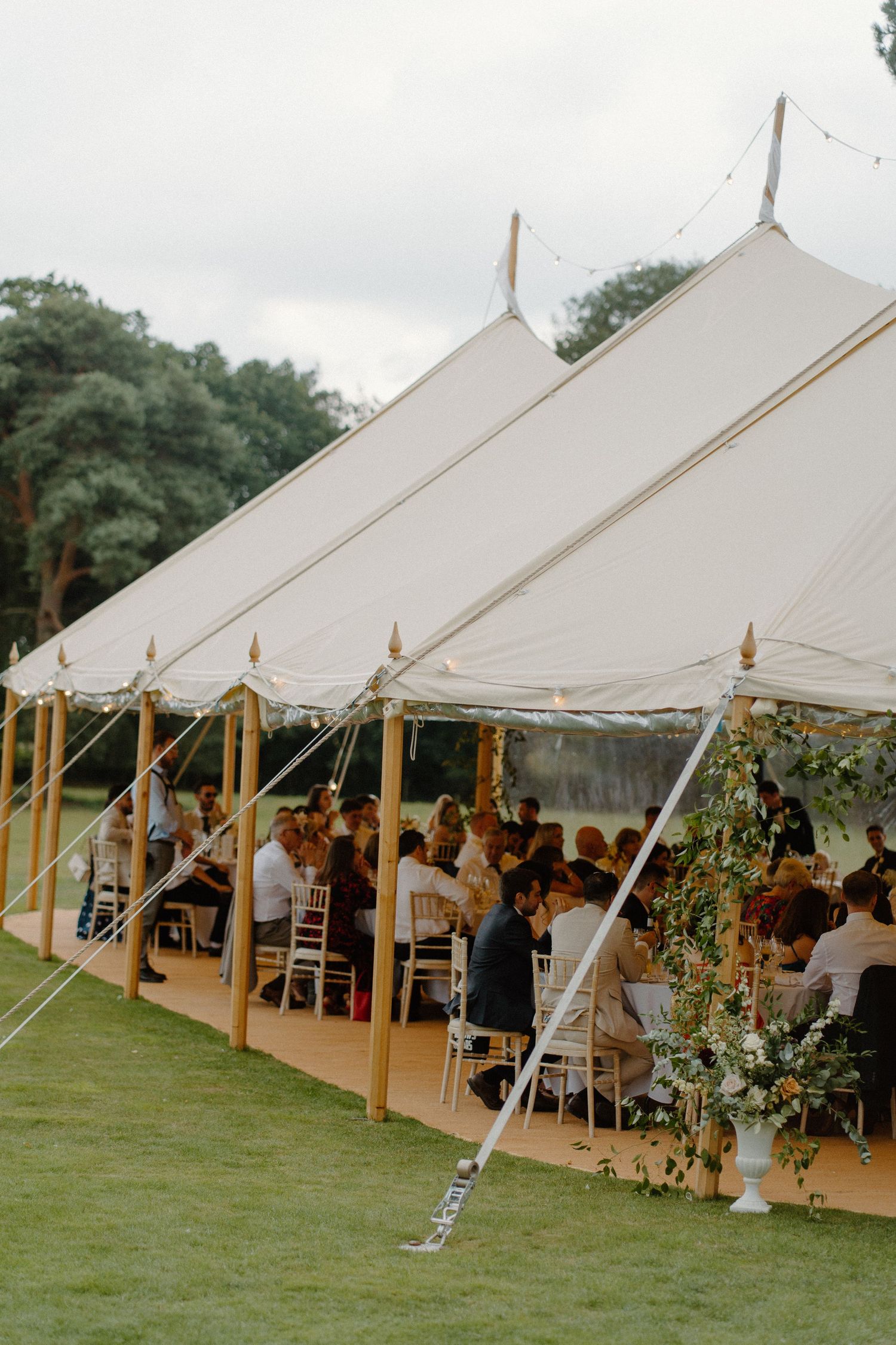 Elegant white sailcloth marquee tent with wooden poles hosting a seated outdoor wedding reception.