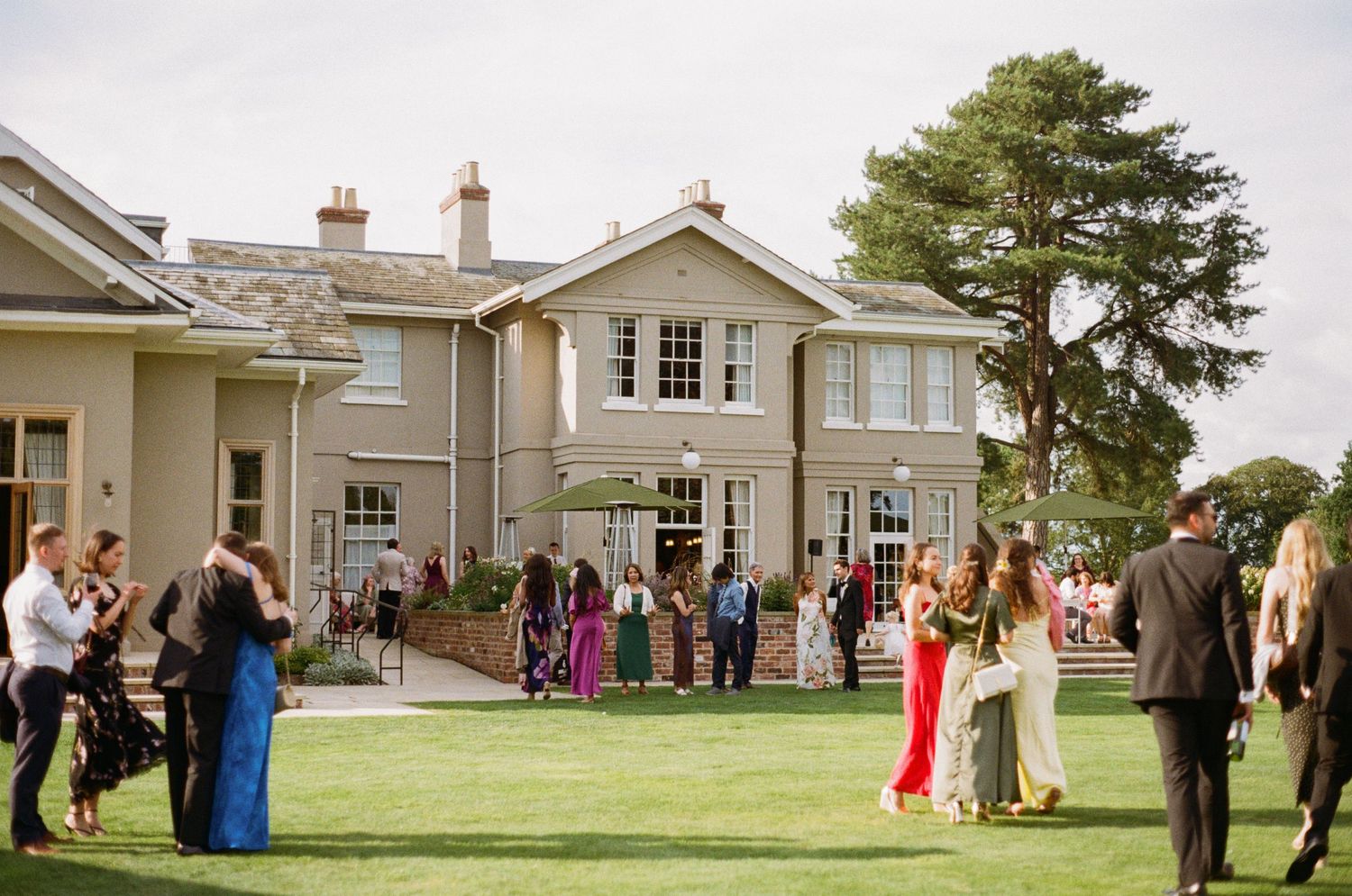 Wedding guests mingling on manicured lawn outside a grand country house venue.
