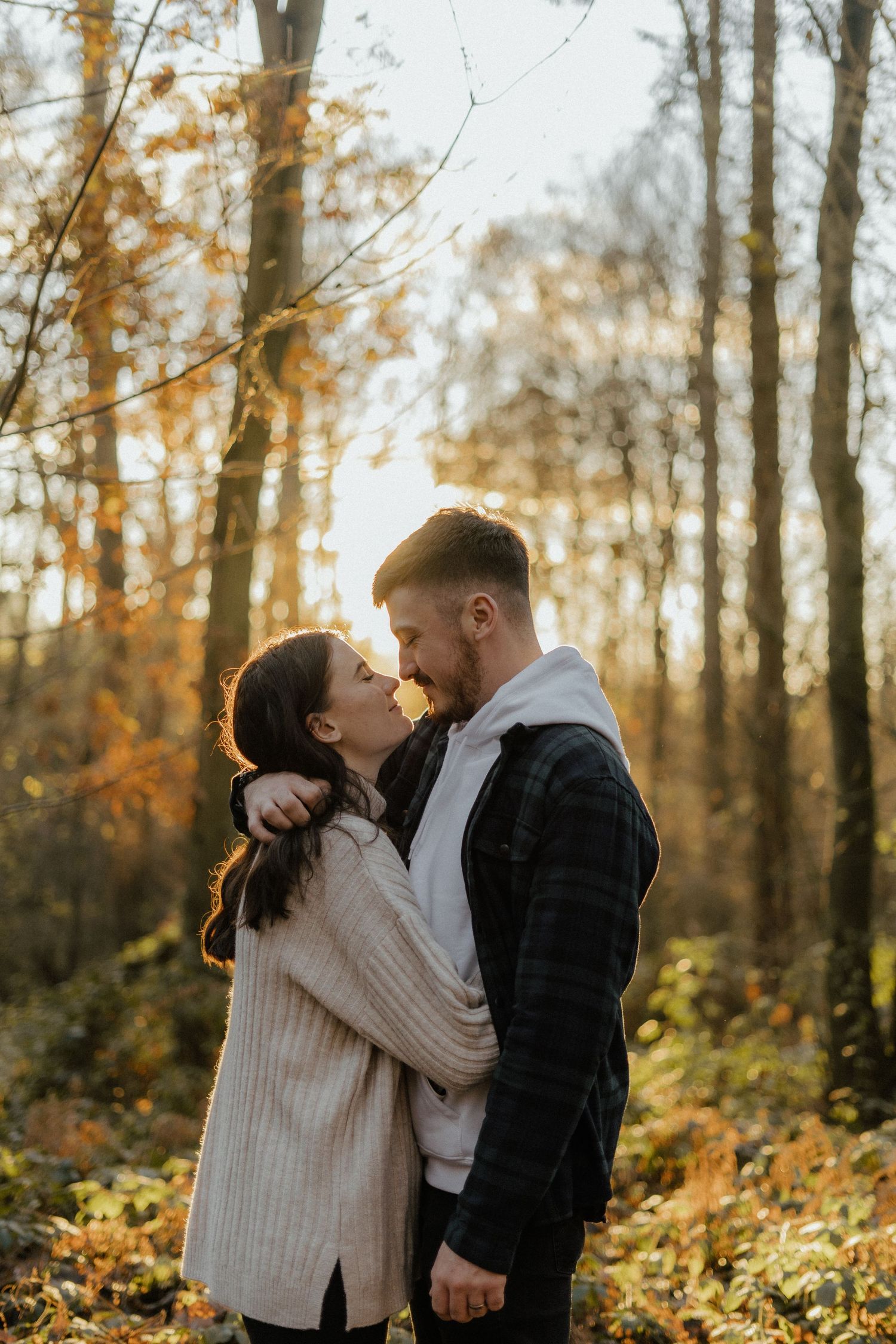 Romantic couple about to kiss in autumn forest with golden foliage and warm sunlight.