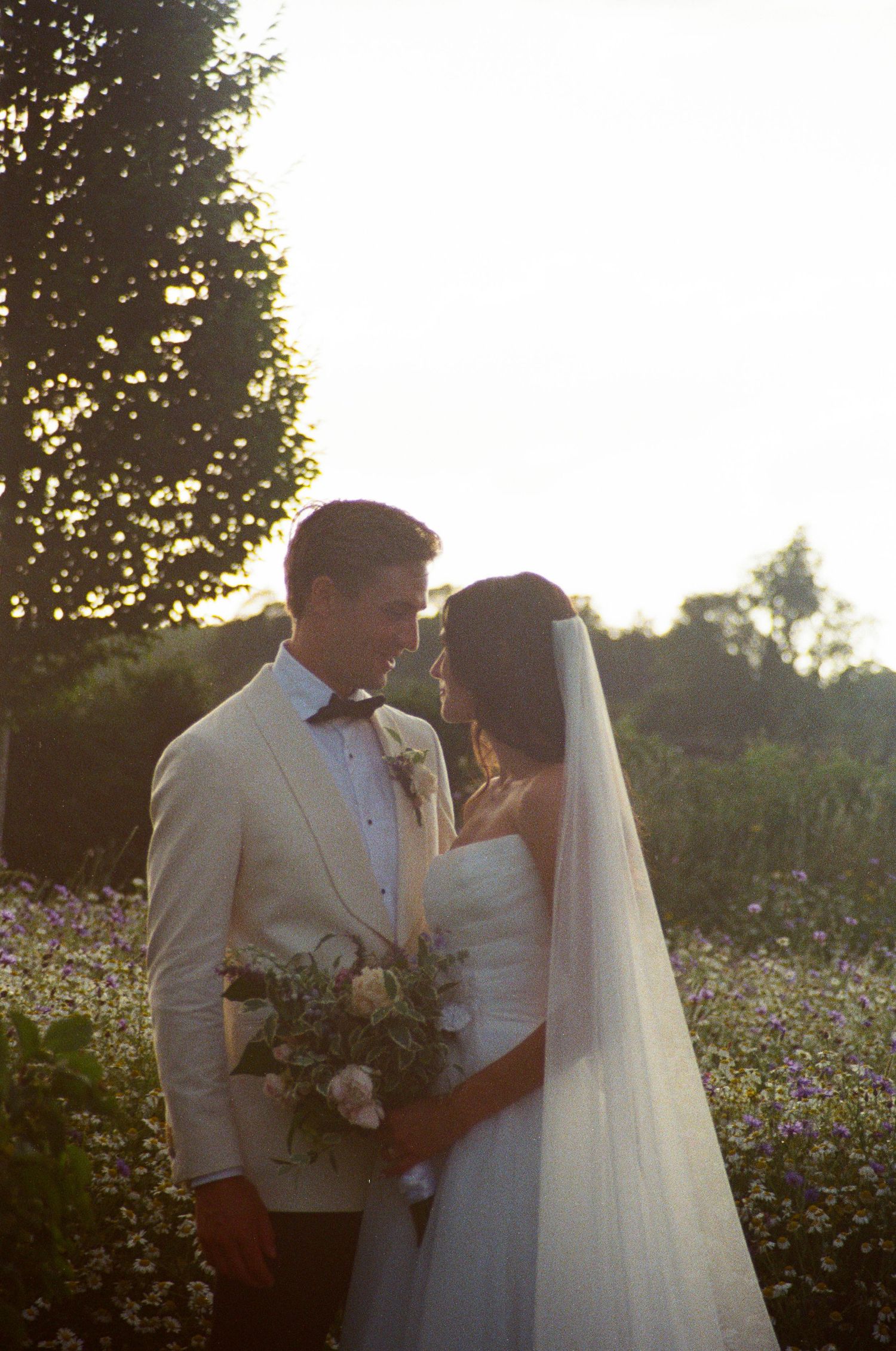 Bride and groom share an intimate moment in a wildflower meadow bathed in golden sunset light.