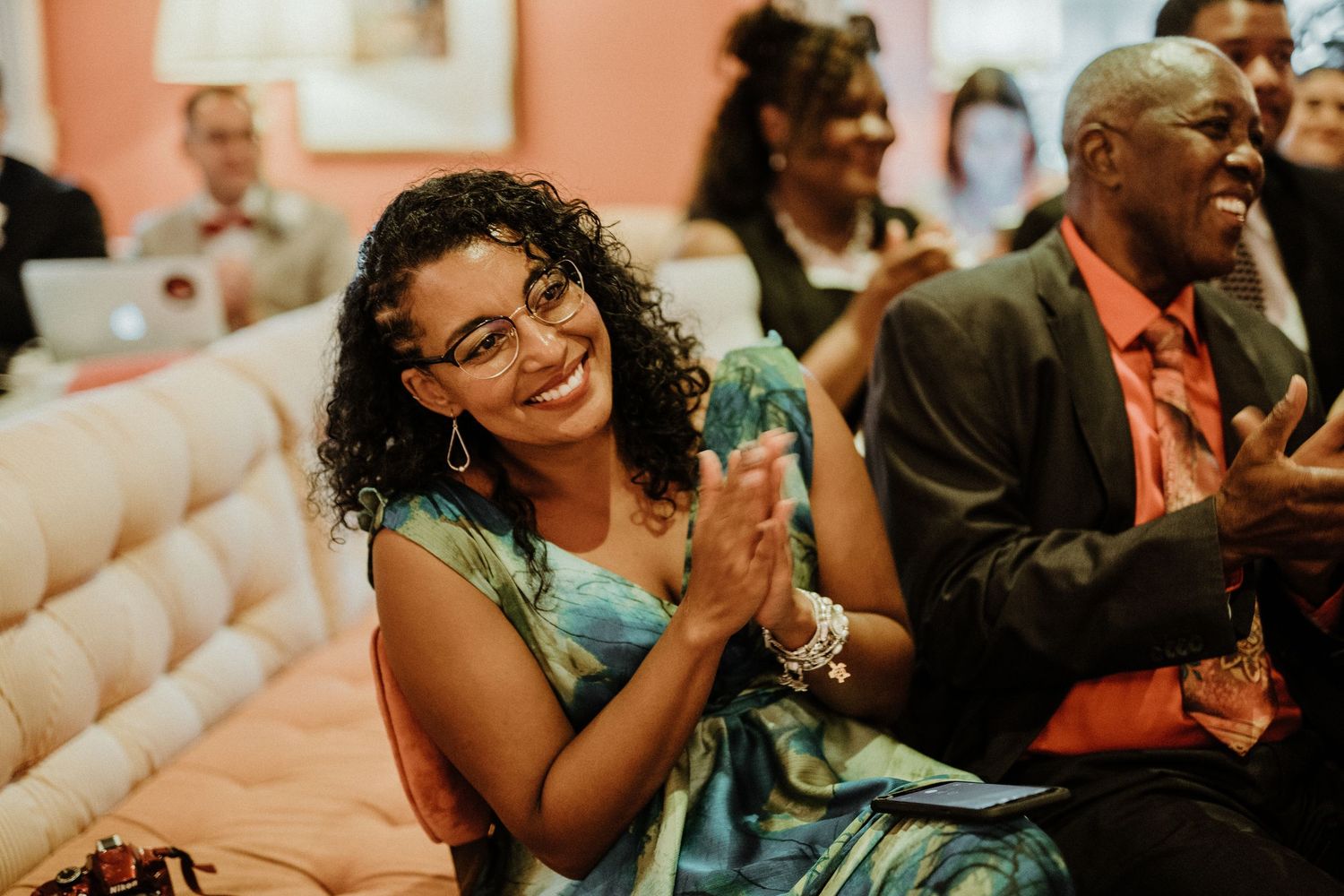Joyful woman in floral dress clapping and smiling at a wedding reception celebration.