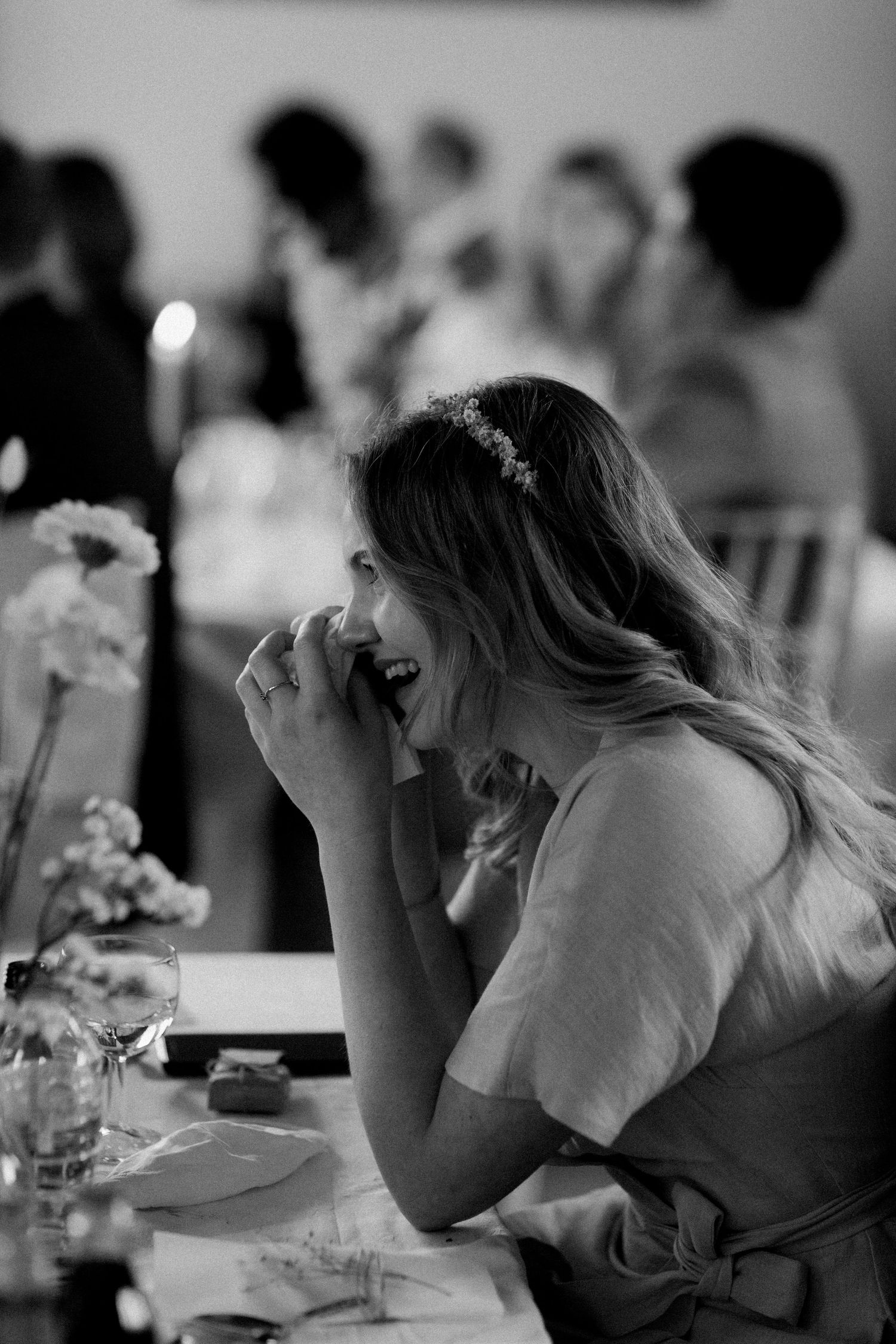 A candid black and white photo of someone laughing at a wedding reception table.