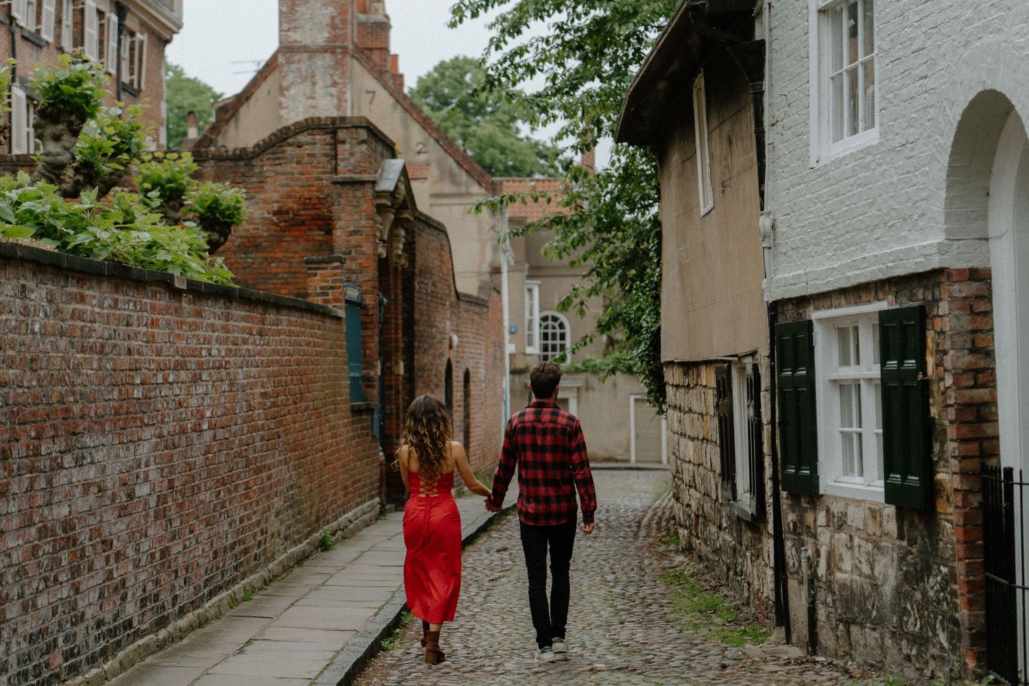 A couple walks down a charming cobblestone alley with historic brick walls and buildings in England.