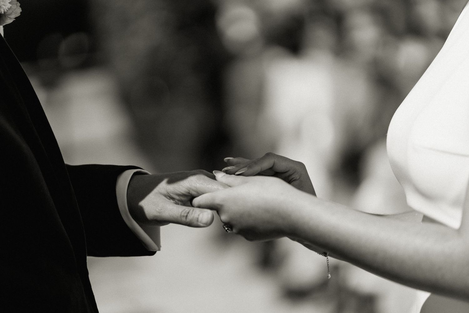 Black and white close-up of groom placing wedding ring on brides hand during the ceremony.