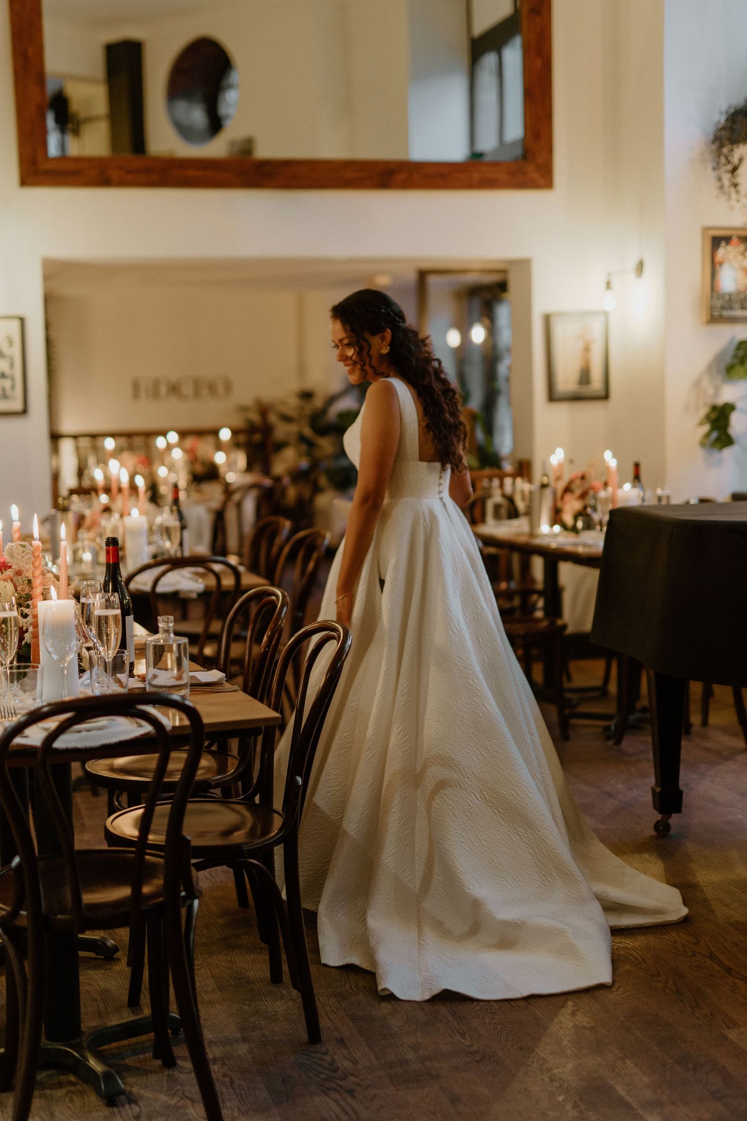 Bride in a white ballgown standing in a candlelit wedding reception venue with bentwood chairs.