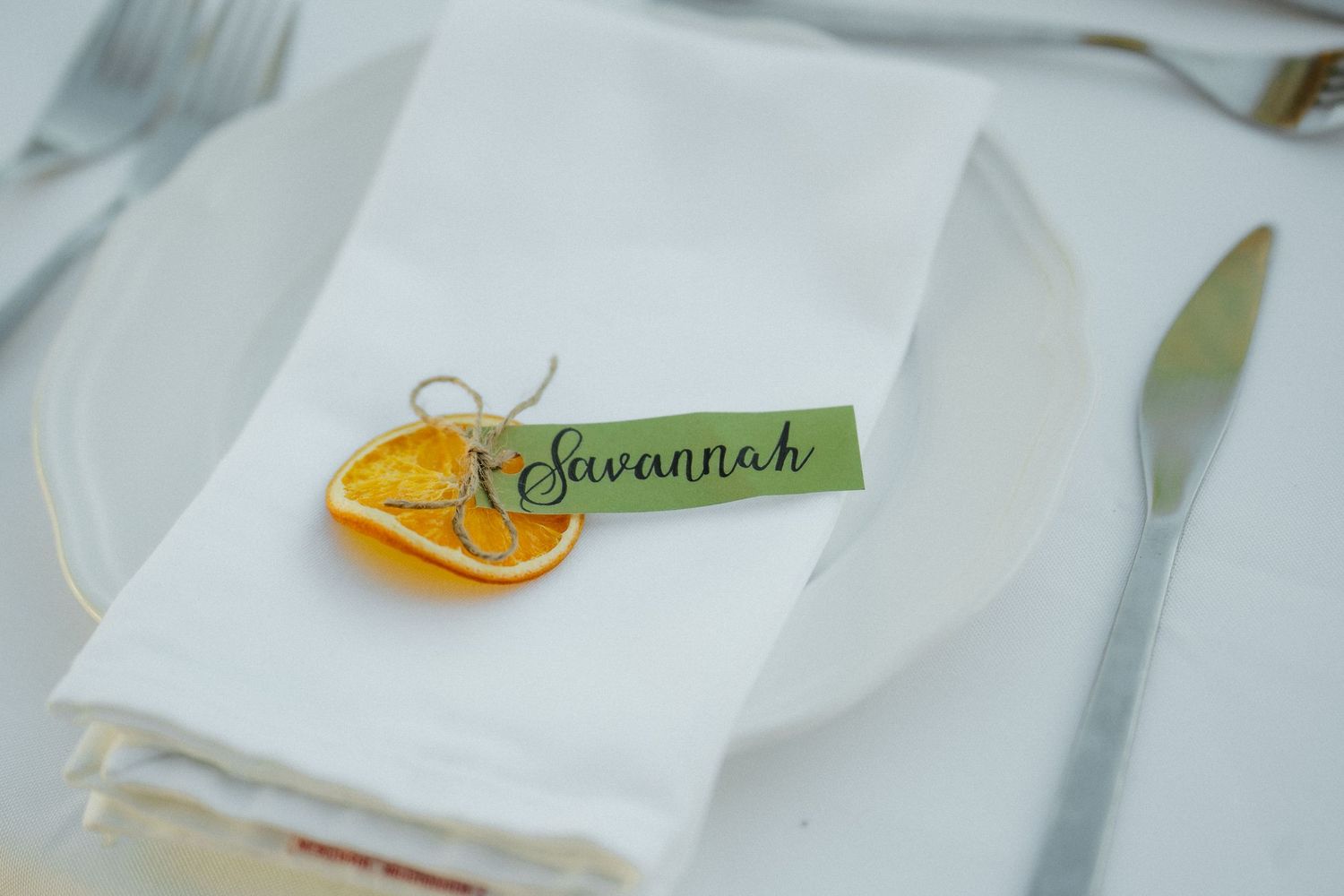 Elegant wedding place setting with dried orange slice and green name card reading Savannah.
