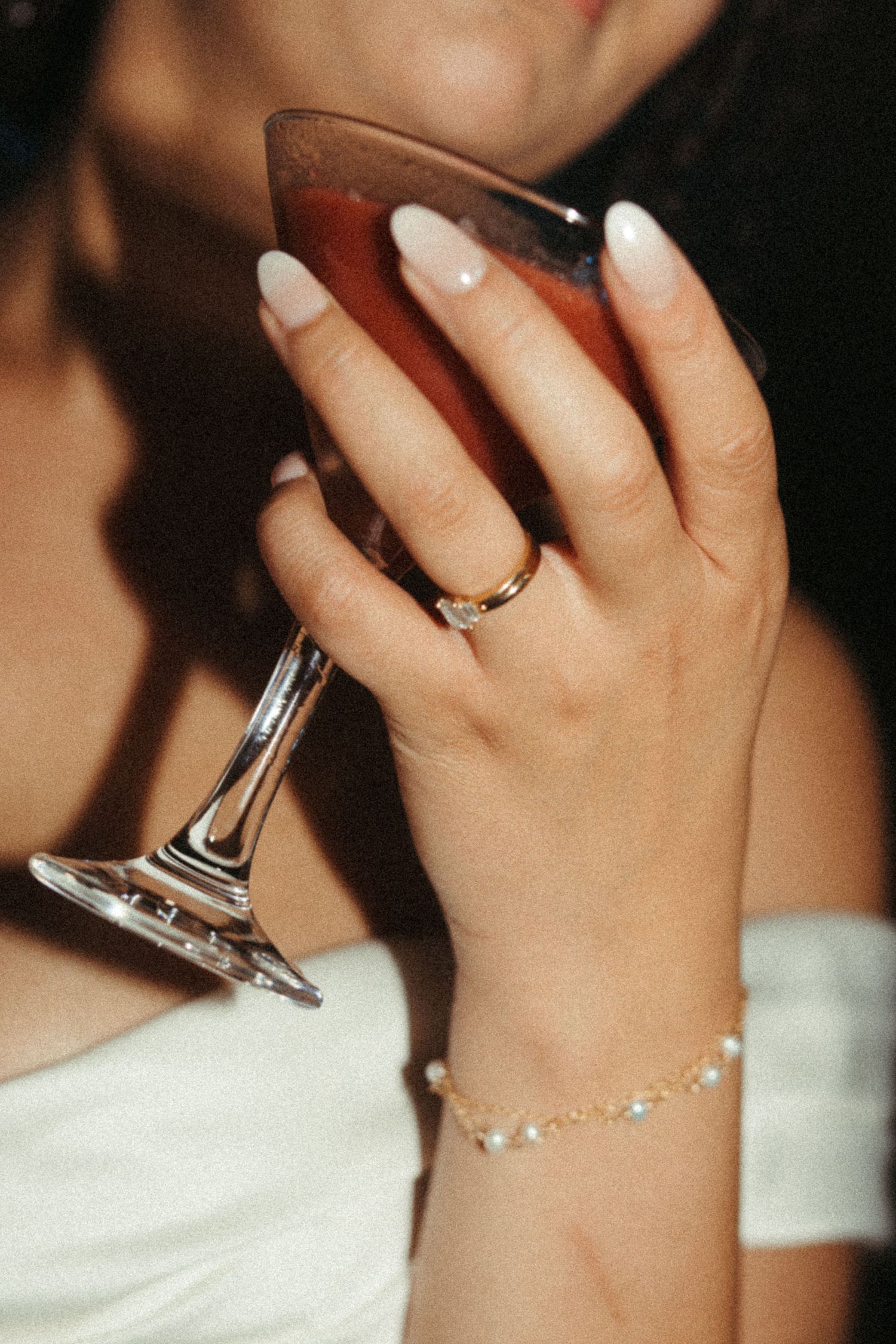Bride wearing engagement ring and pearl bracelet holding a cocktail glass.