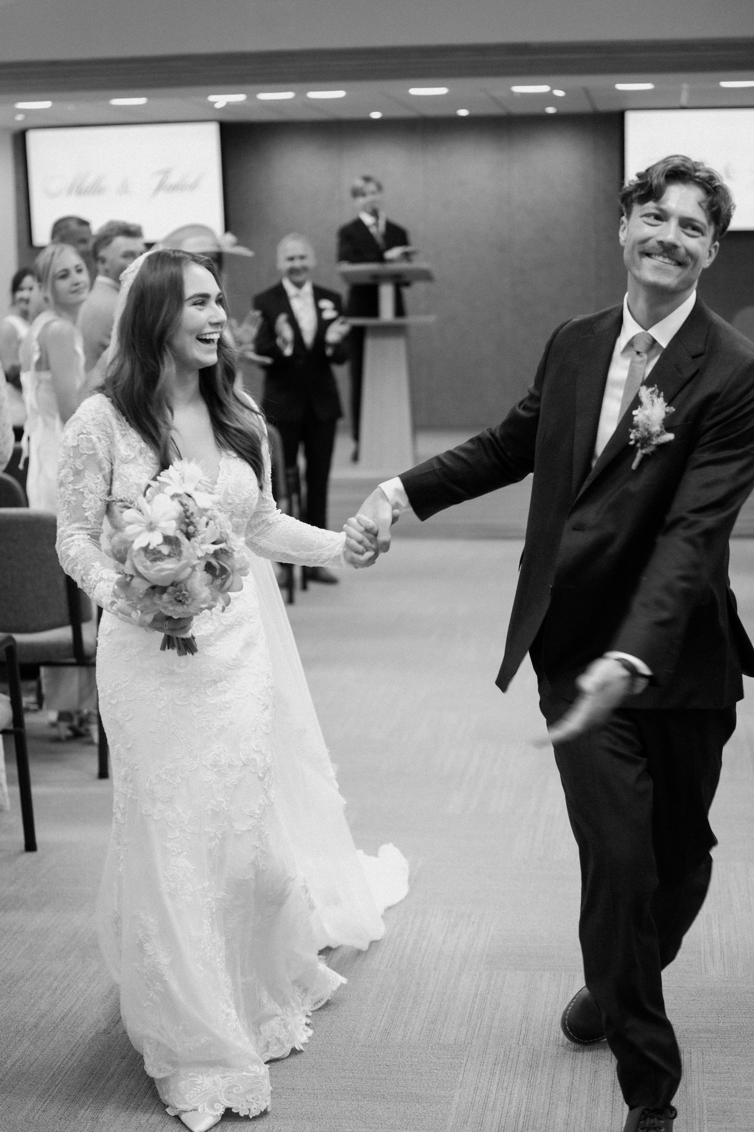 Joyful bride and groom walking down the aisle after wedding ceremony in black and white photo.