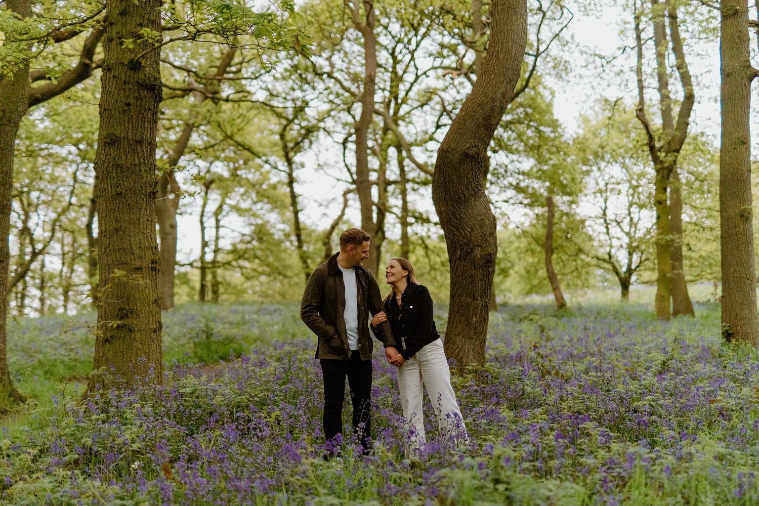 Couple walking hand in hand through a bluebell woodland forest in spring.