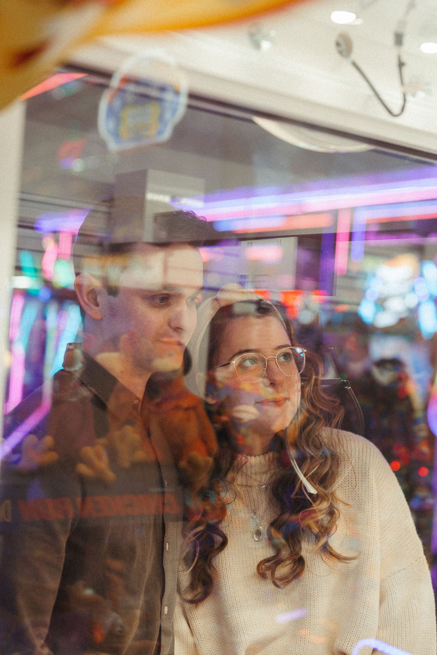 Couple reflected in arcade game glass, bathed in colorful neon lights together.