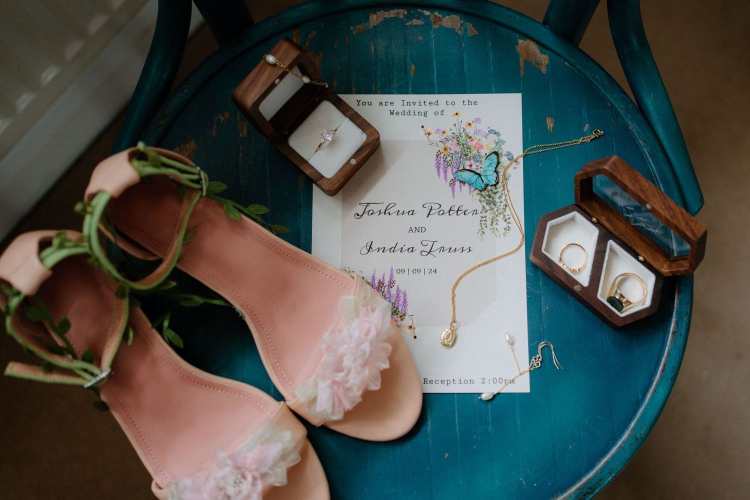 Wedding details including pink ballet flats, a stationery suite and perfume bottles arranged on a teal blue surface.
