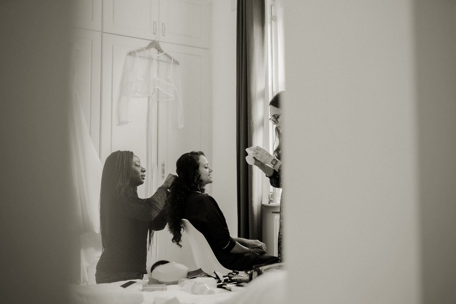 Black and white photo of bride getting hair done by stylist before wedding ceremony.