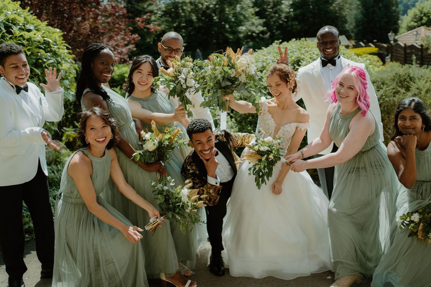 Wedding party celebrating outdoors with bridesmaids in sage green dresses and groomsmen in white tuxedos.