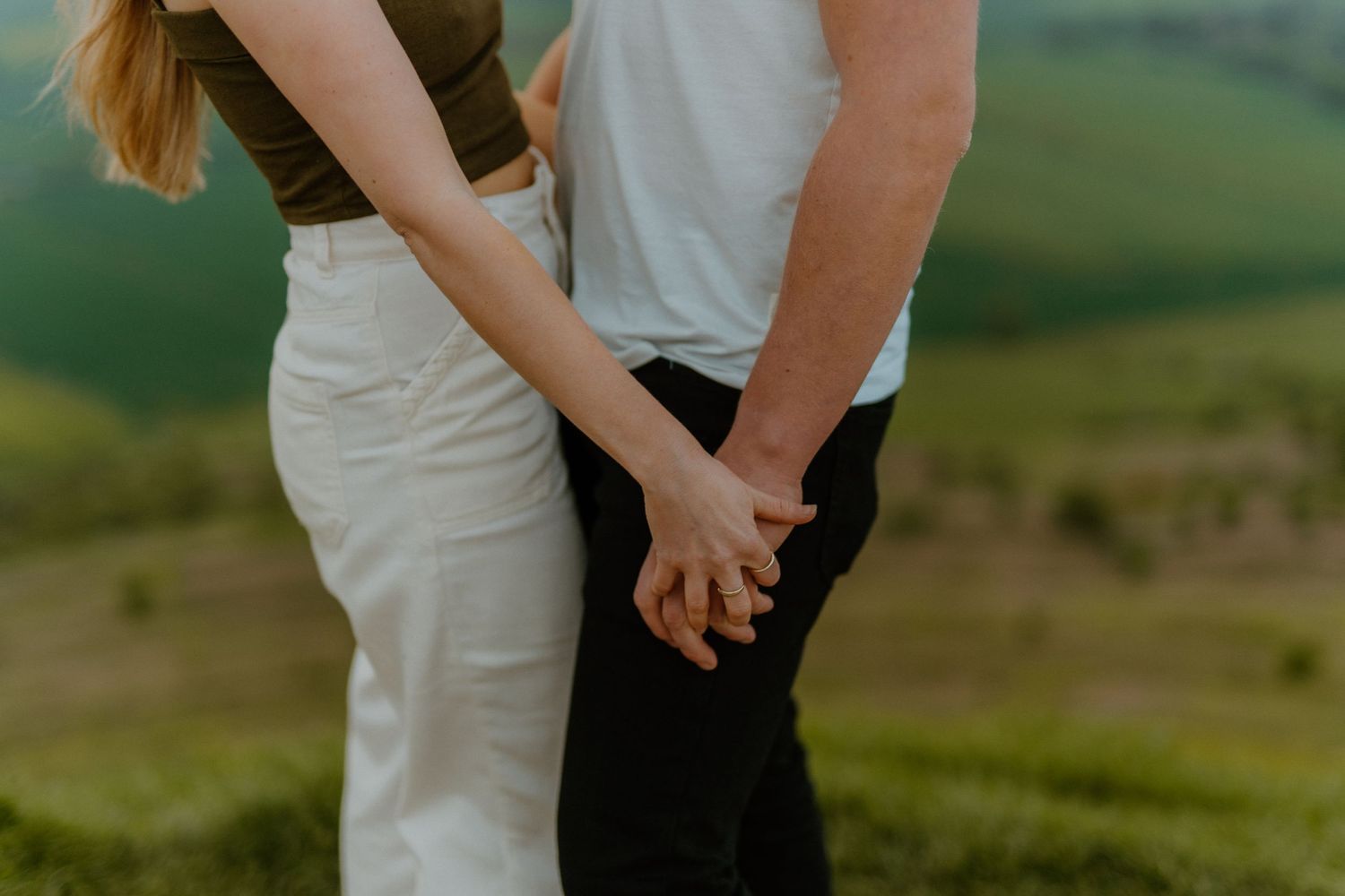 Close-up of couple holding hands together against a soft green blurred background.
