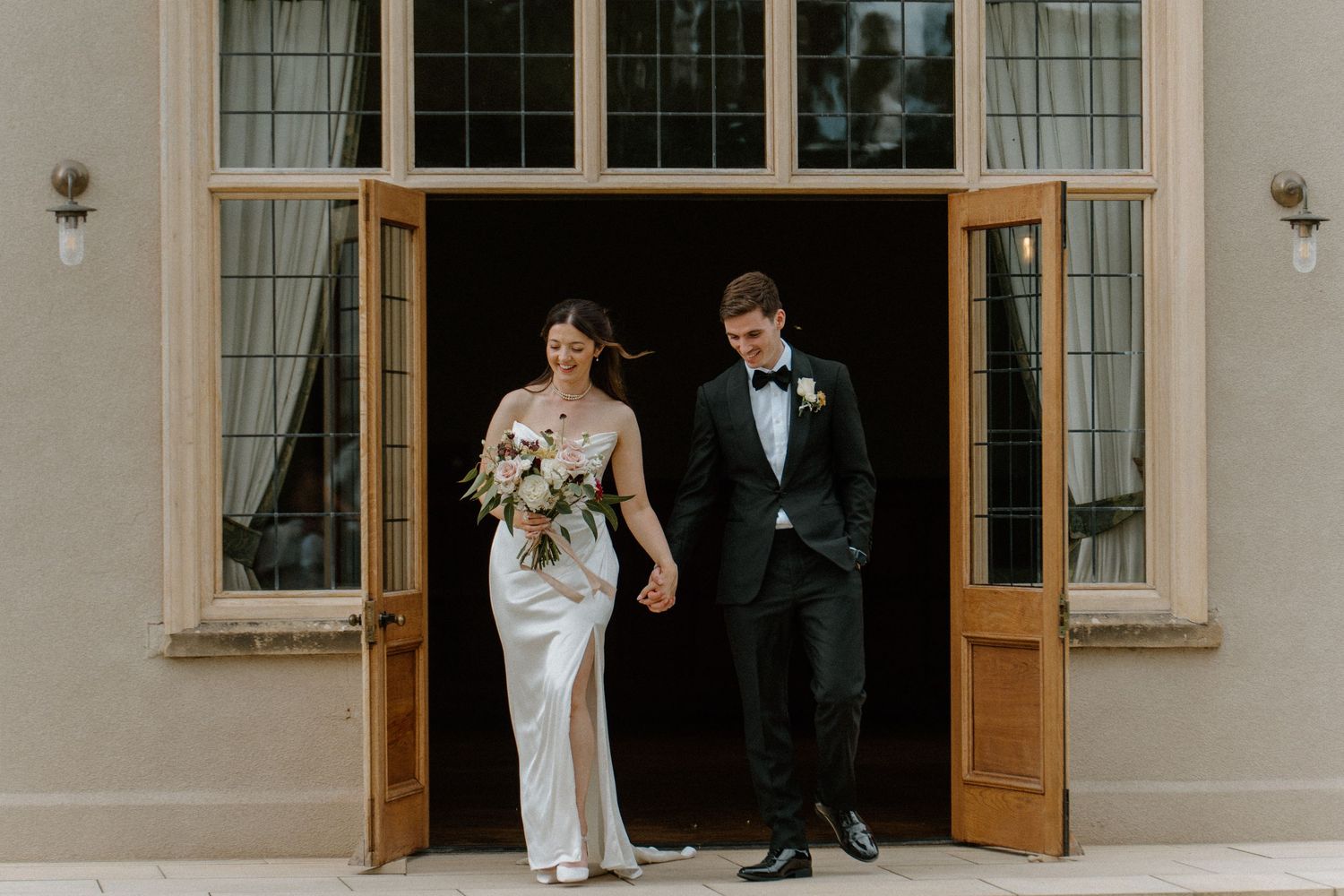 Bride and groom walking hand in hand through grand double doors of a stately wedding venue.