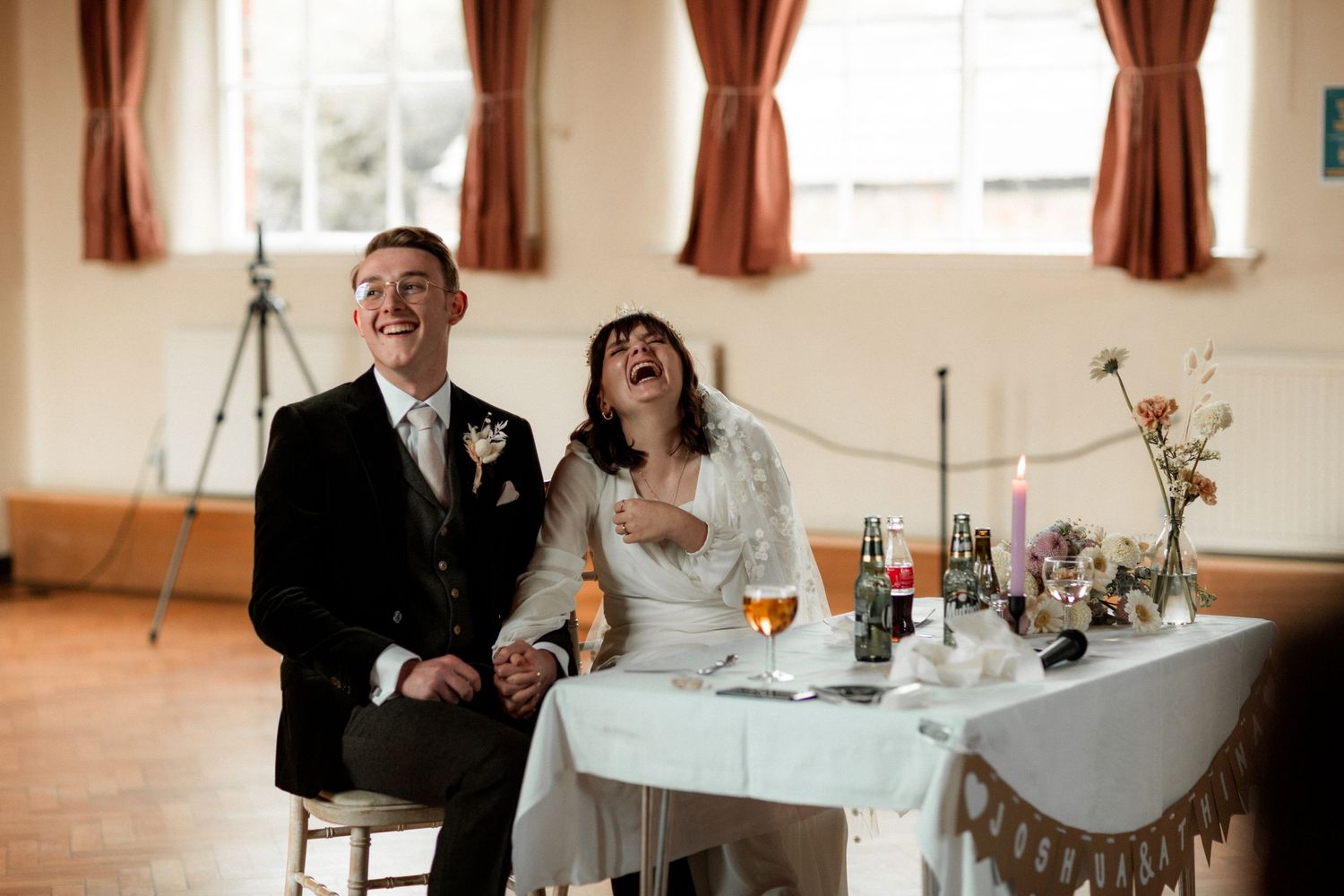 A candid reception moment with laughter at a wedding table decorated with flowers.